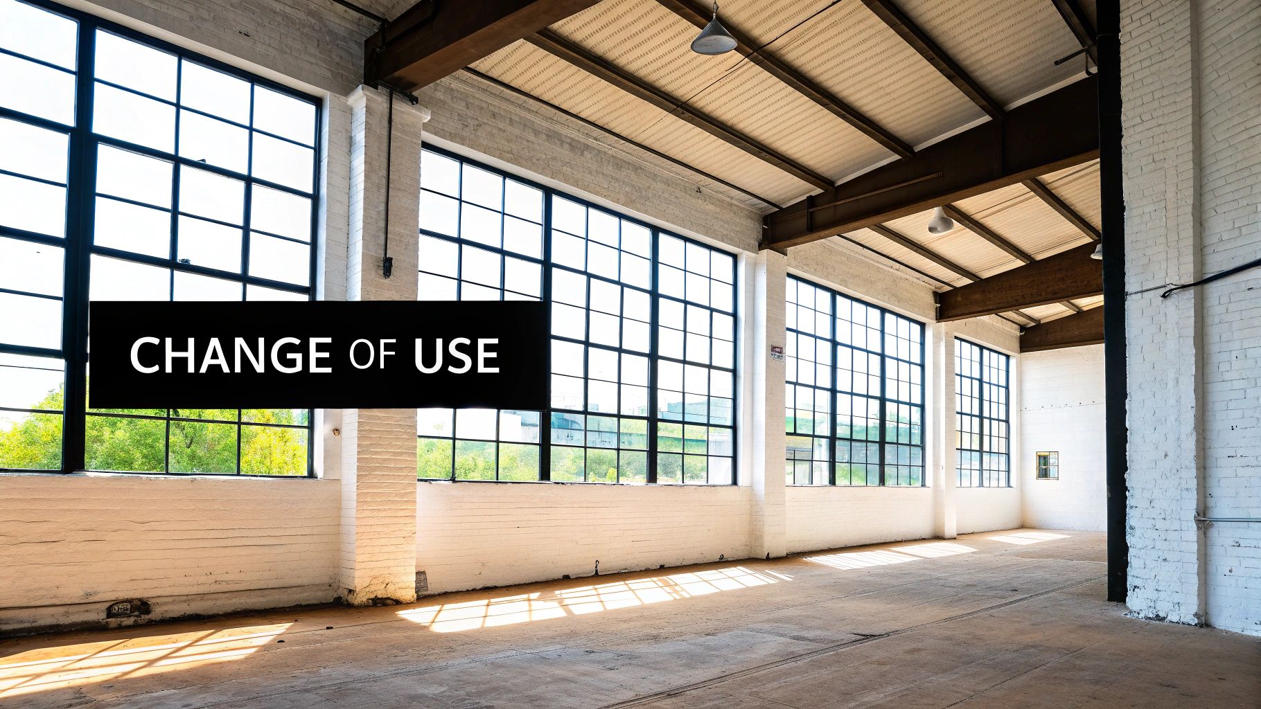 An empty, sunlit industrial warehouse with large windows and white brick walls, featuring a 'CHANGE OF USE' sign.