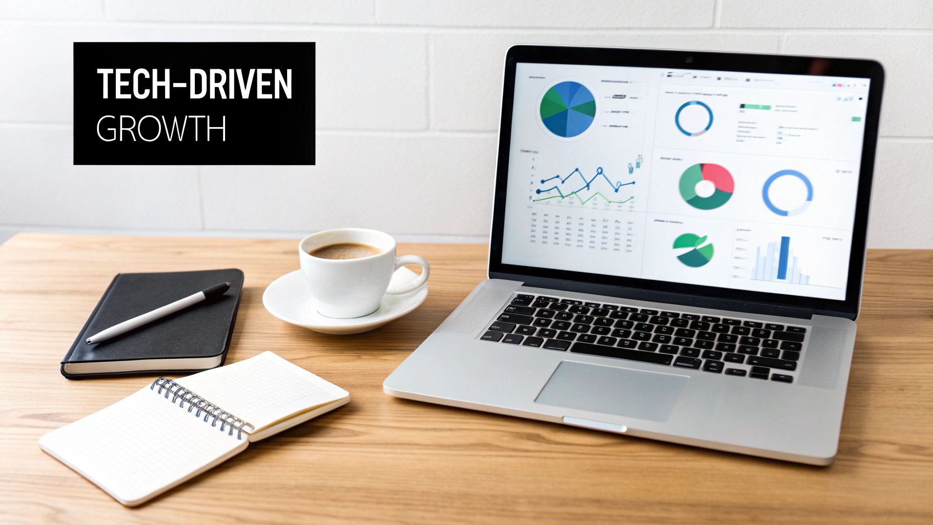A laptop screen displaying vibrant business analytics charts alongside coffee, notebooks, and a 'TECH-DRIVEN GROWTH' sign.