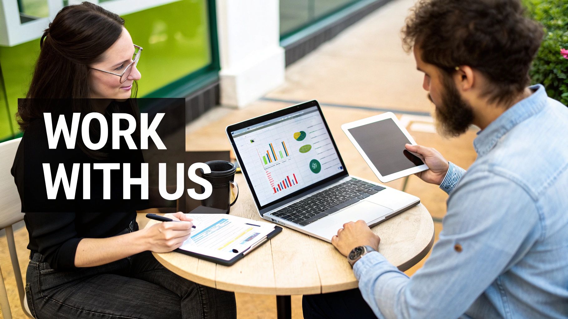 Two professionals collaborating at an outdoor table with a laptop and tablet, text 'WORK WITH US'.