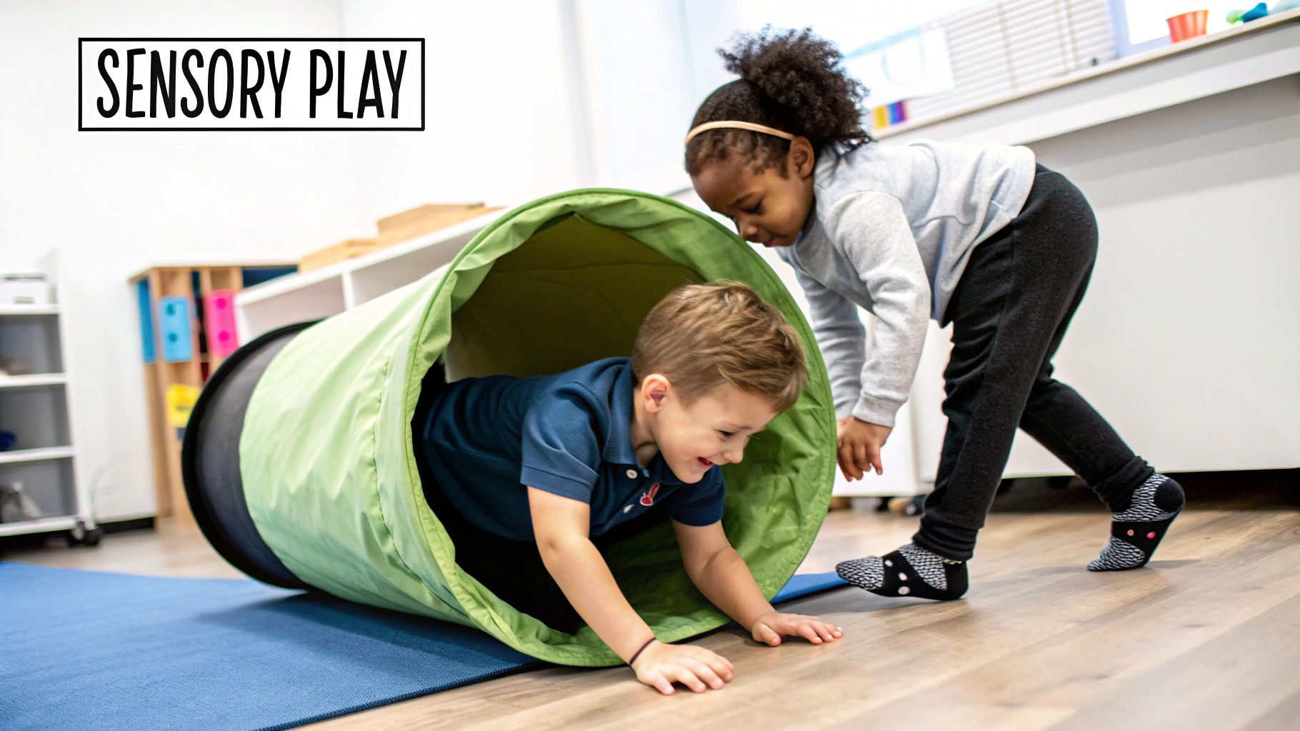 Two happy children engaged in sensory play, one crawling out of a green tunnel, the other watching.