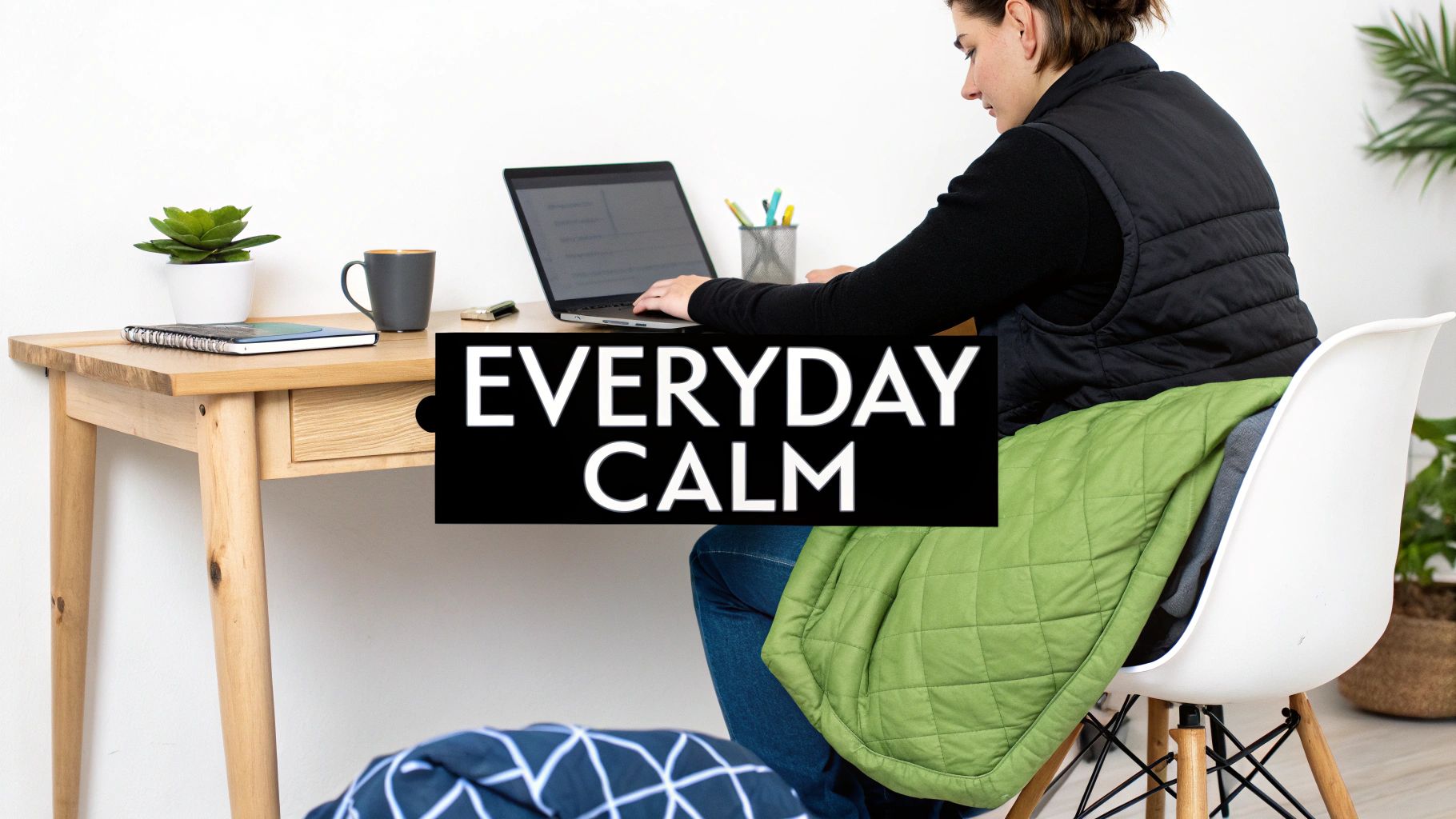 Person working on a laptop at a wooden desk, covered with a green weighted blanket for calm.