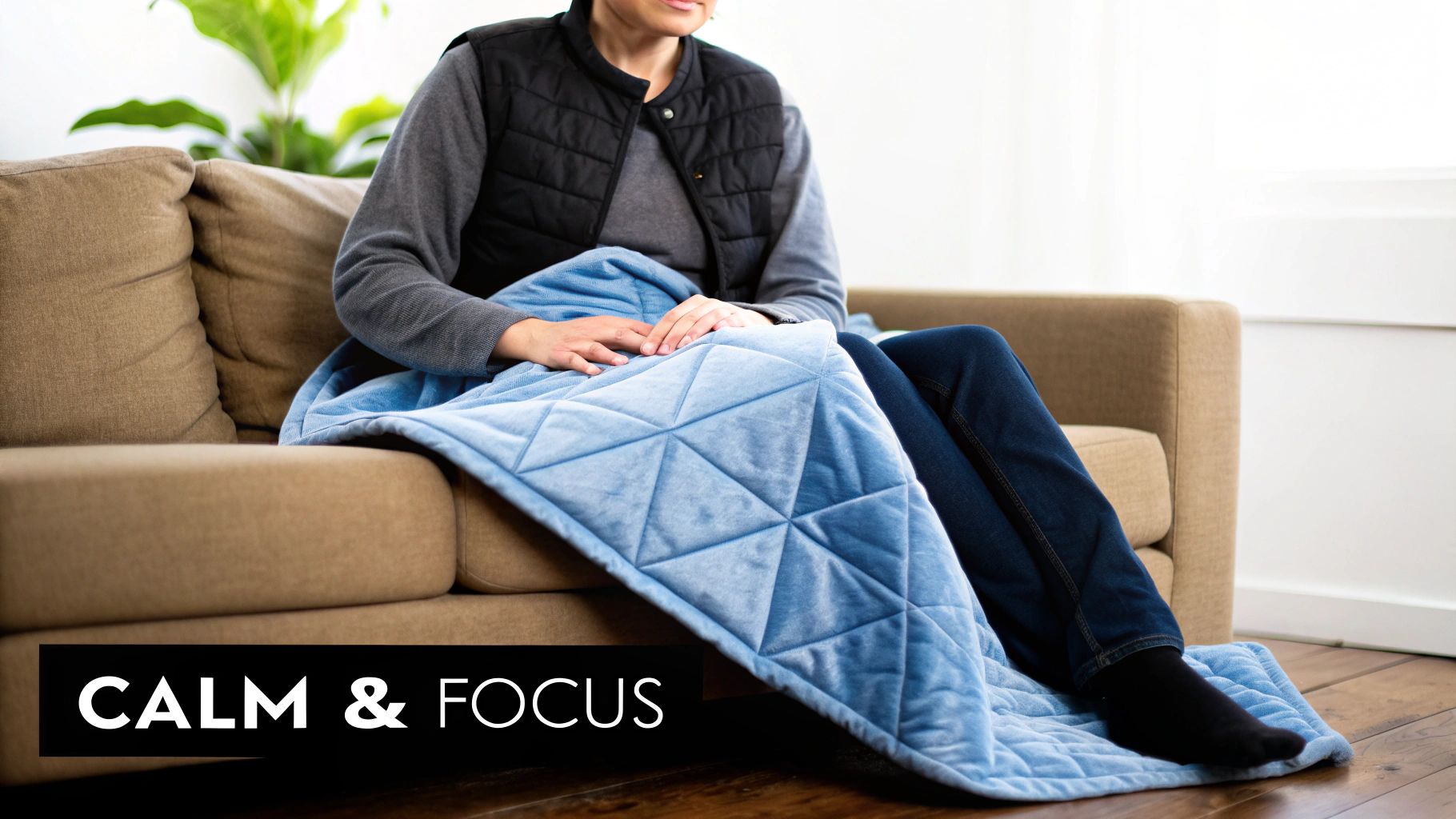A person relaxing on a sofa, covered by a blue quilted weighted lap blanket for comfort.