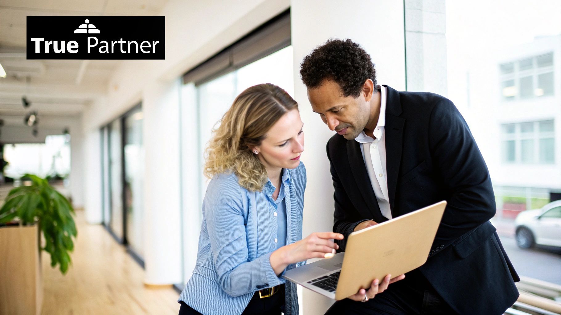 Two diverse business professionals, a man and a woman, collaborating on a laptop in a modern office.