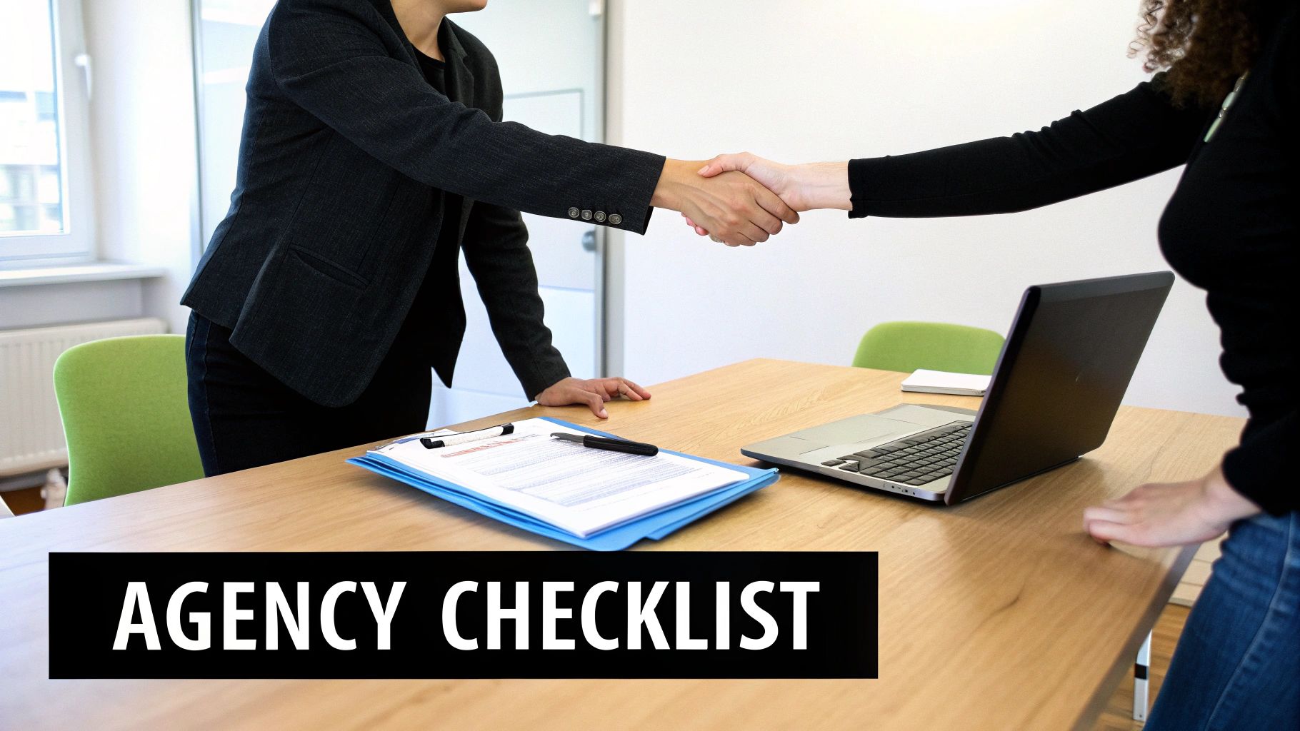 Two business professionals shaking hands over a desk with a laptop and documents, signifying agreement or partnership.