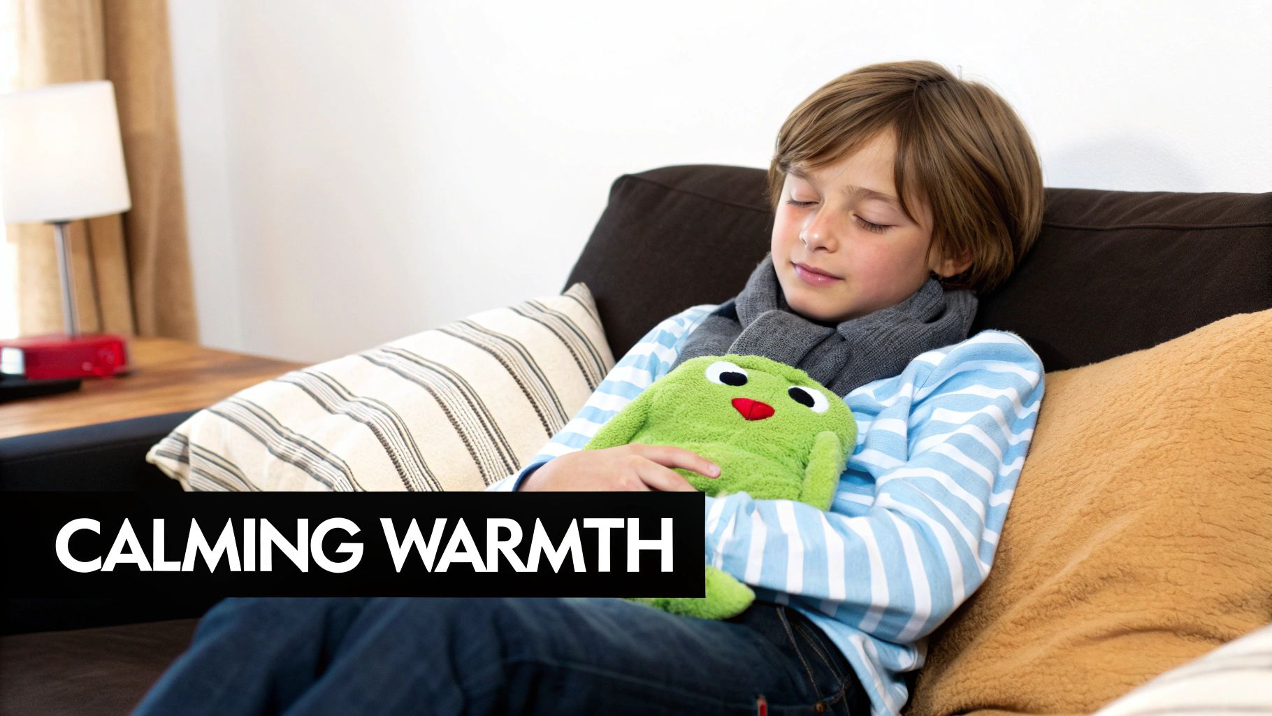 A young boy rests peacefully on a couch with closed eyes, cuddling a green frog heat pack.