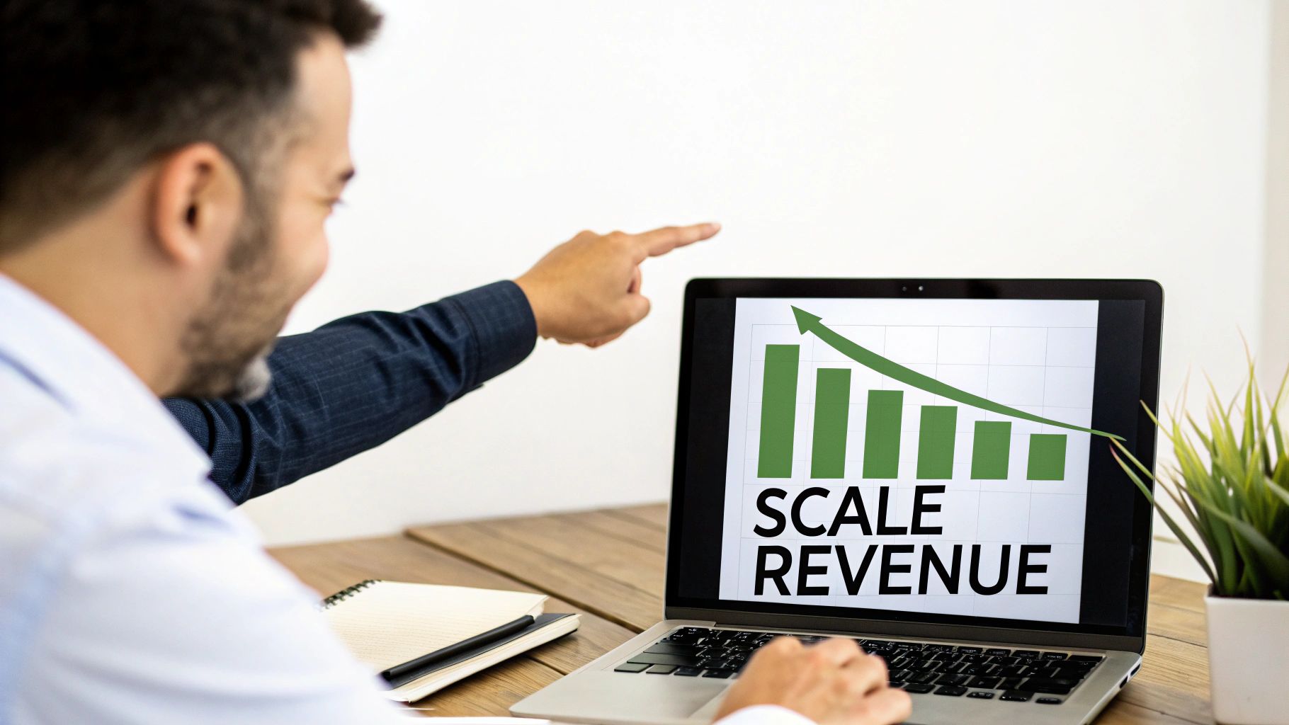A man in a white shirt points at a laptop screen displaying a 'Scale Revenue' chart with an upward trend.