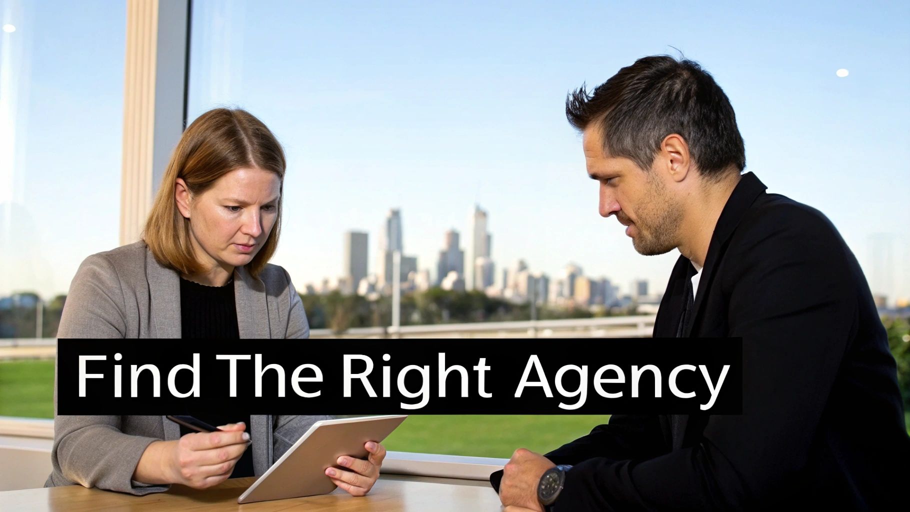 Two business professionals discuss content on a tablet in a modern office with a city view.