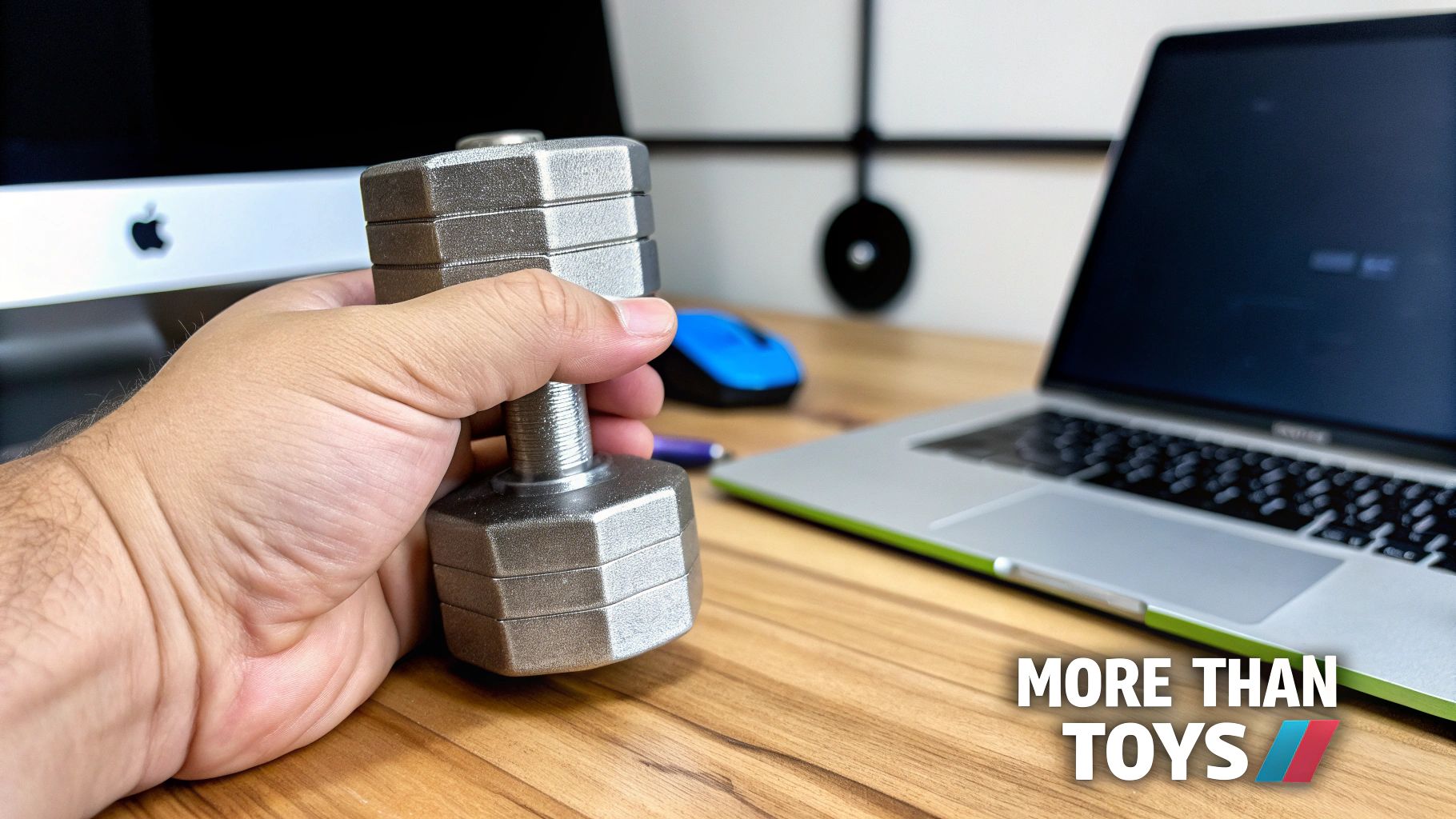 A person's hand holds a small silver adjustable dumbbell at a desk with computer equipment.