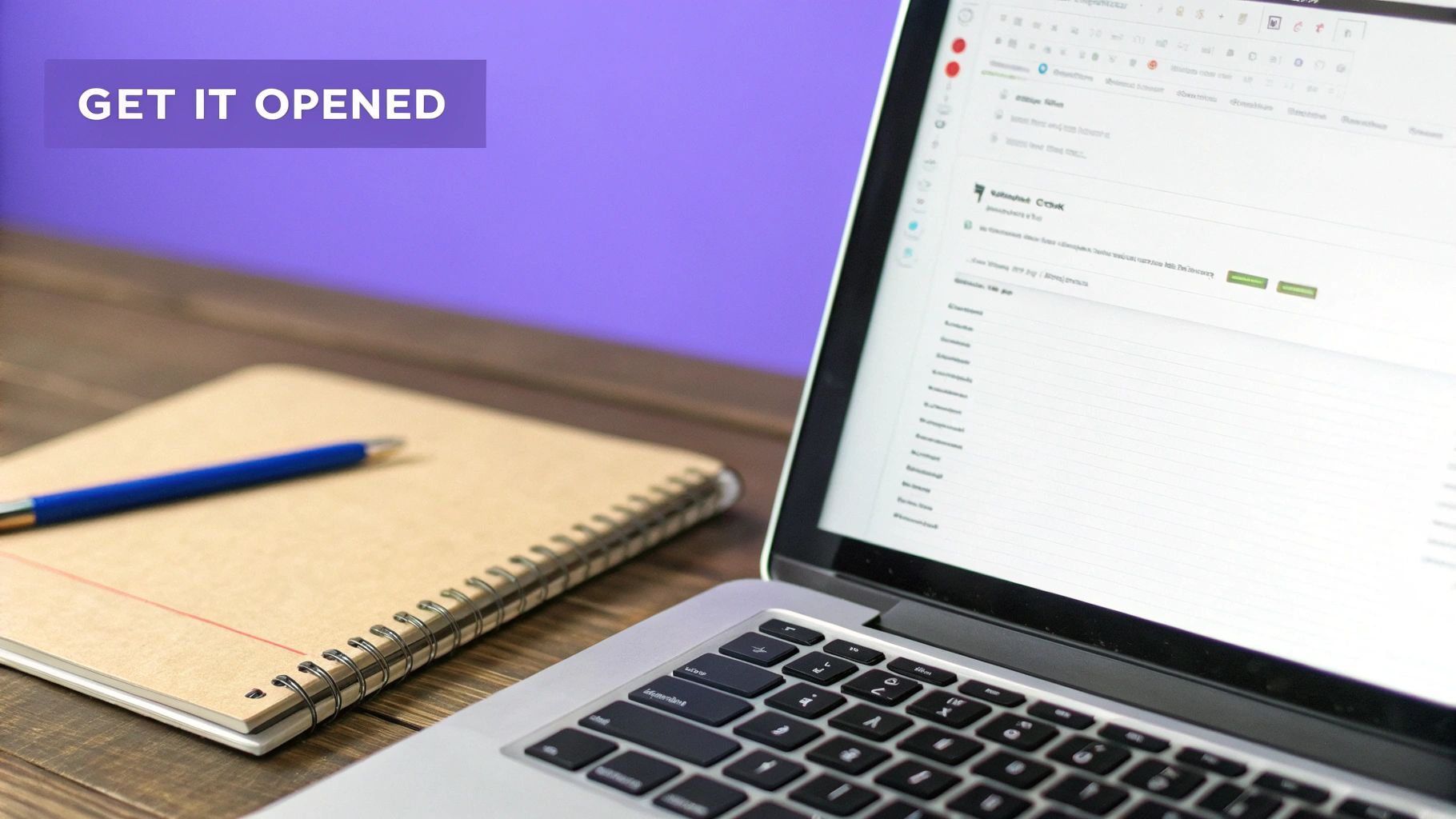 Workspace scene with a laptop, spiral notebook, and blue pen on a dark wooden desk.