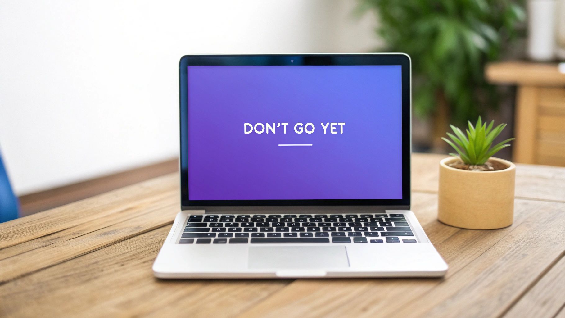 Laptop displaying don't go yet message on purple gradient screen on wooden desk