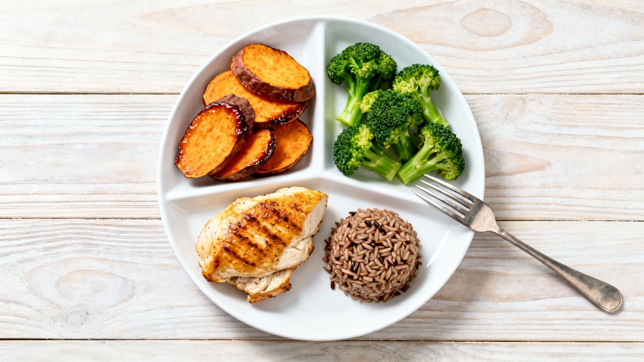 A healthy post-workout meal featuring grilled chicken, roasted sweet potatoes, steamed broccoli, and wild rice.