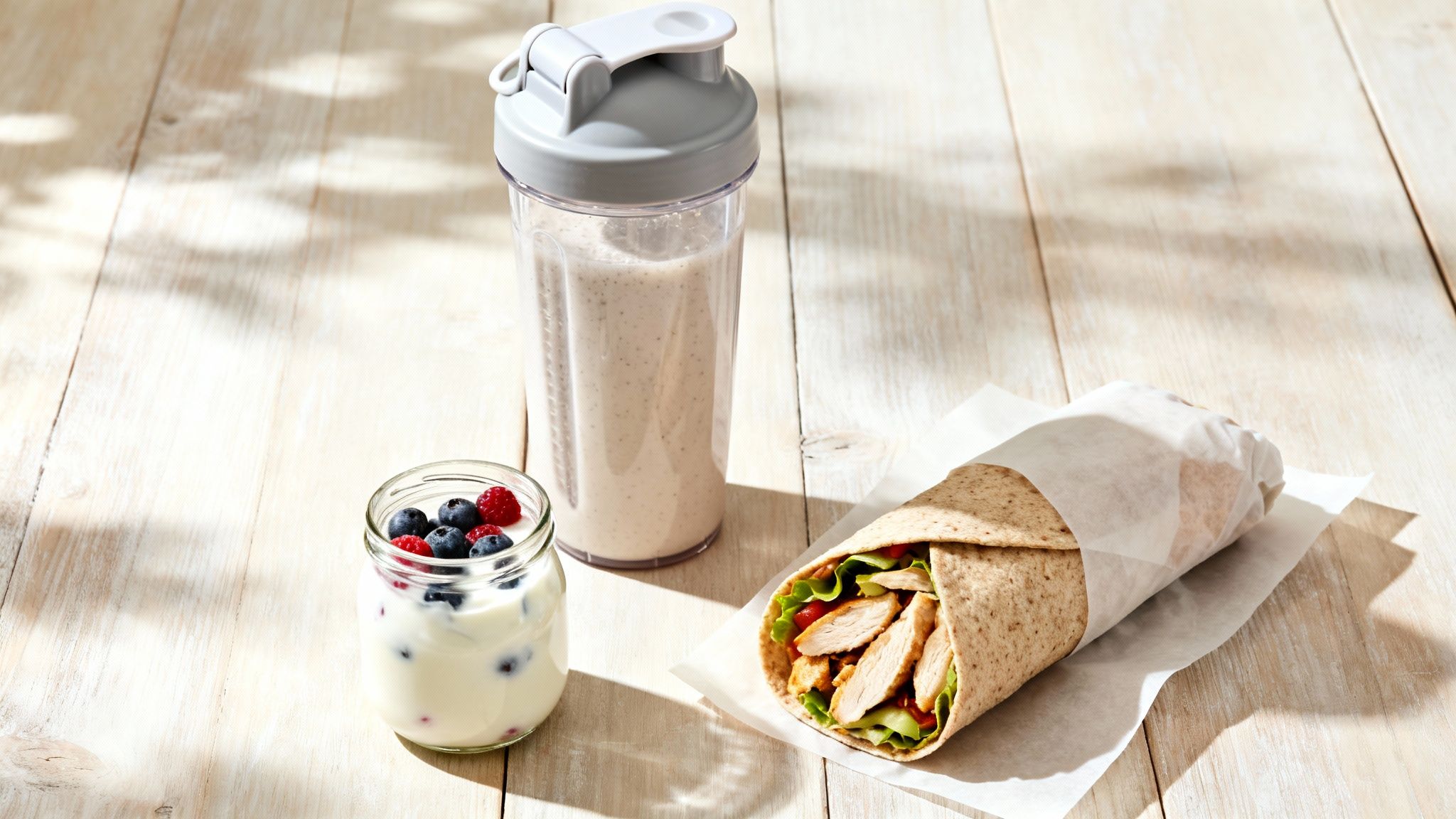 A healthy post-workout meal featuring a chicken wrap, berry yogurt, and protein shake on a wooden table.