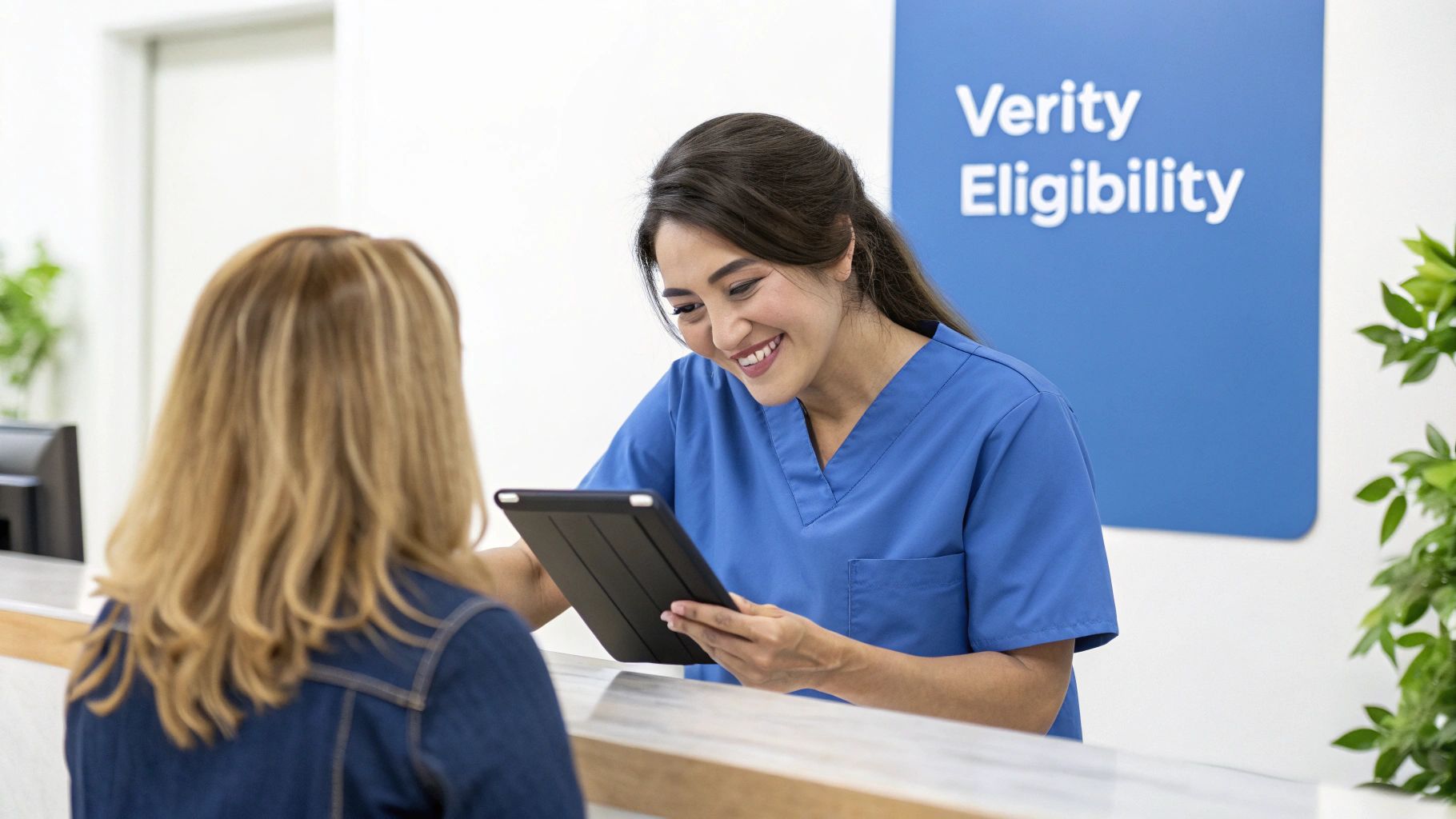 A cheerful nurse in blue scrubs helps a patient at a medical reception desk, using a tablet for eligibility.