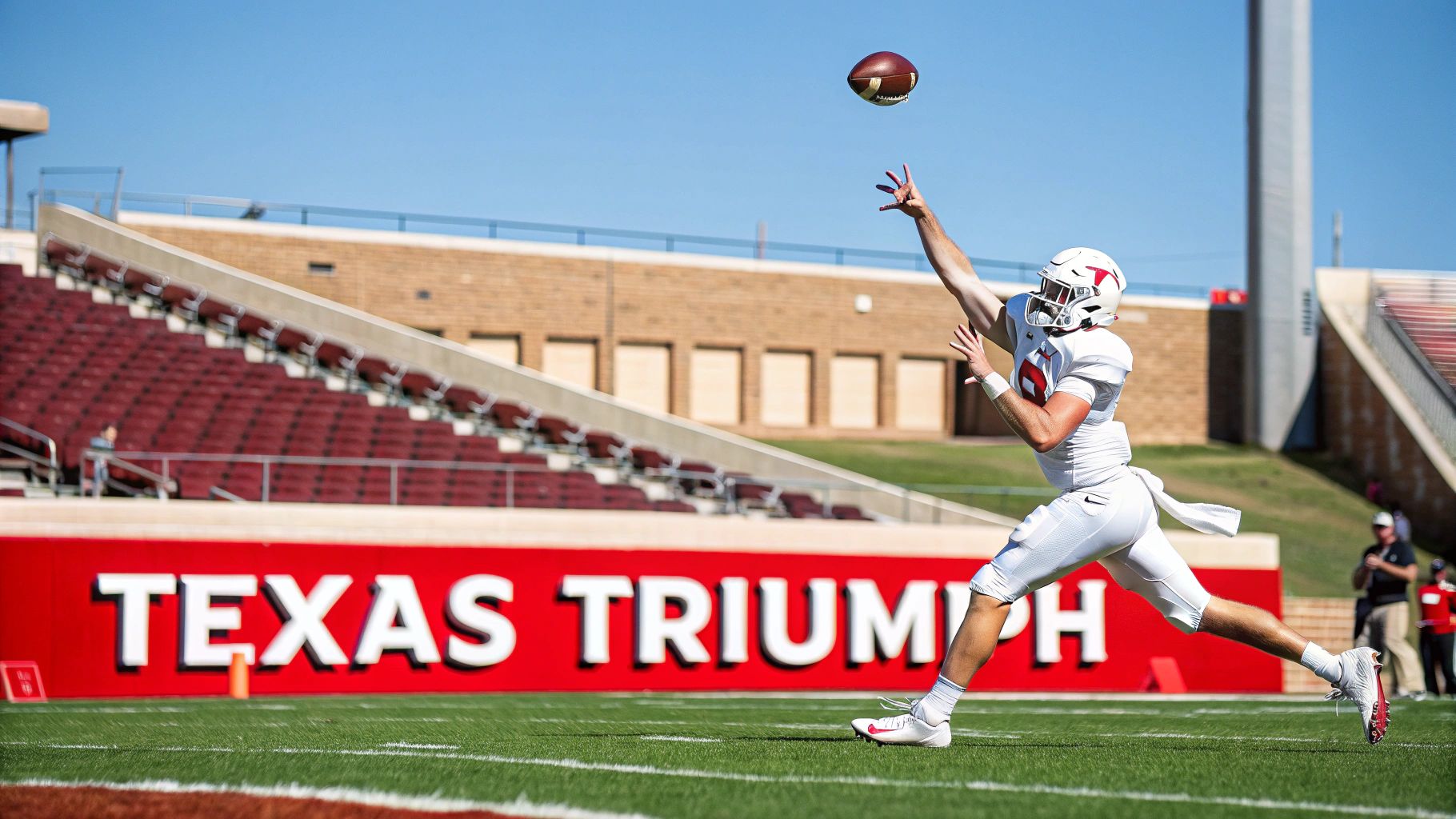 A football player in a white uniform reaches for a football during a game at a stadium.