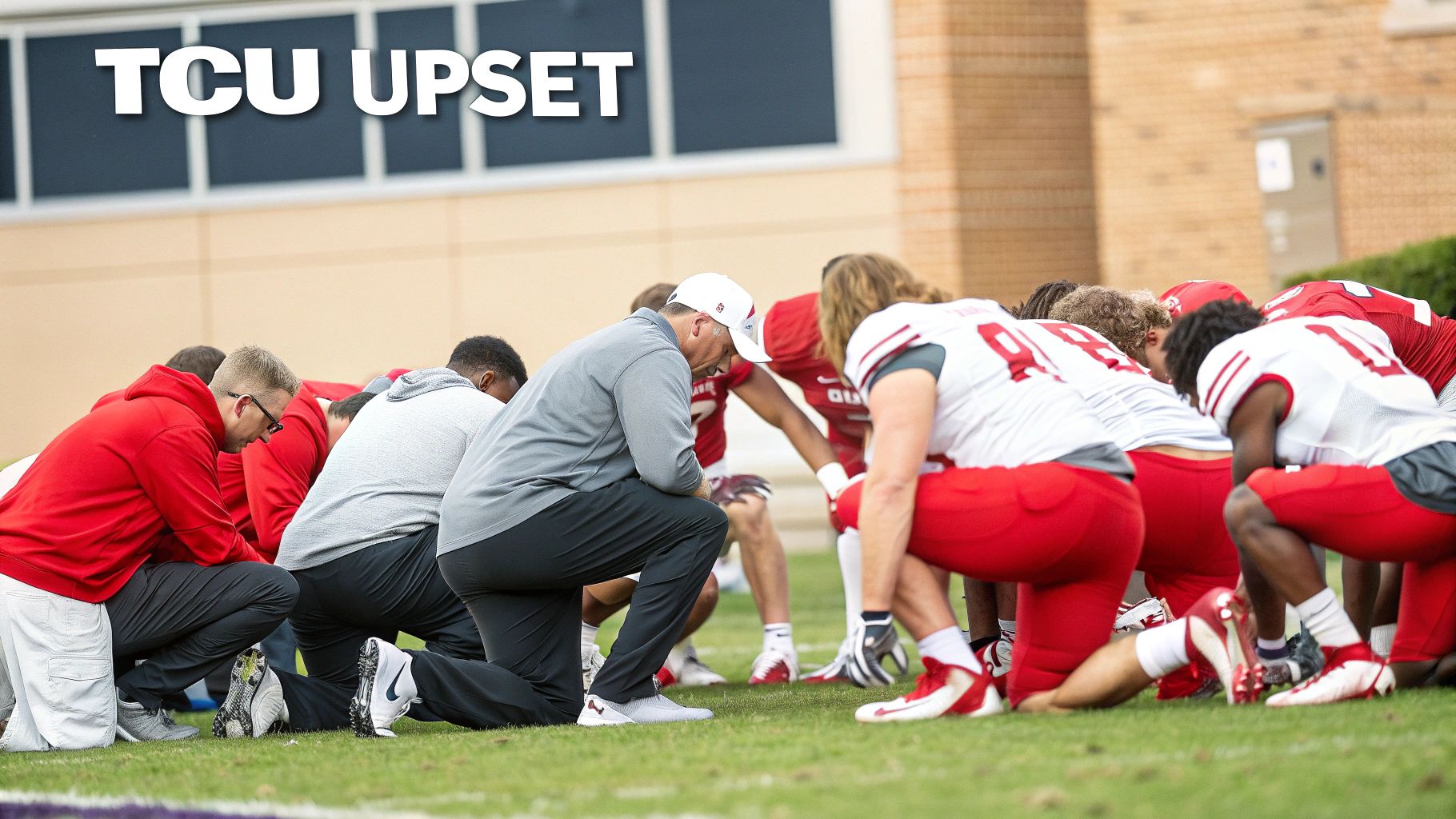 Football players and coaches in red and white uniforms kneeling in a huddle on a field.
