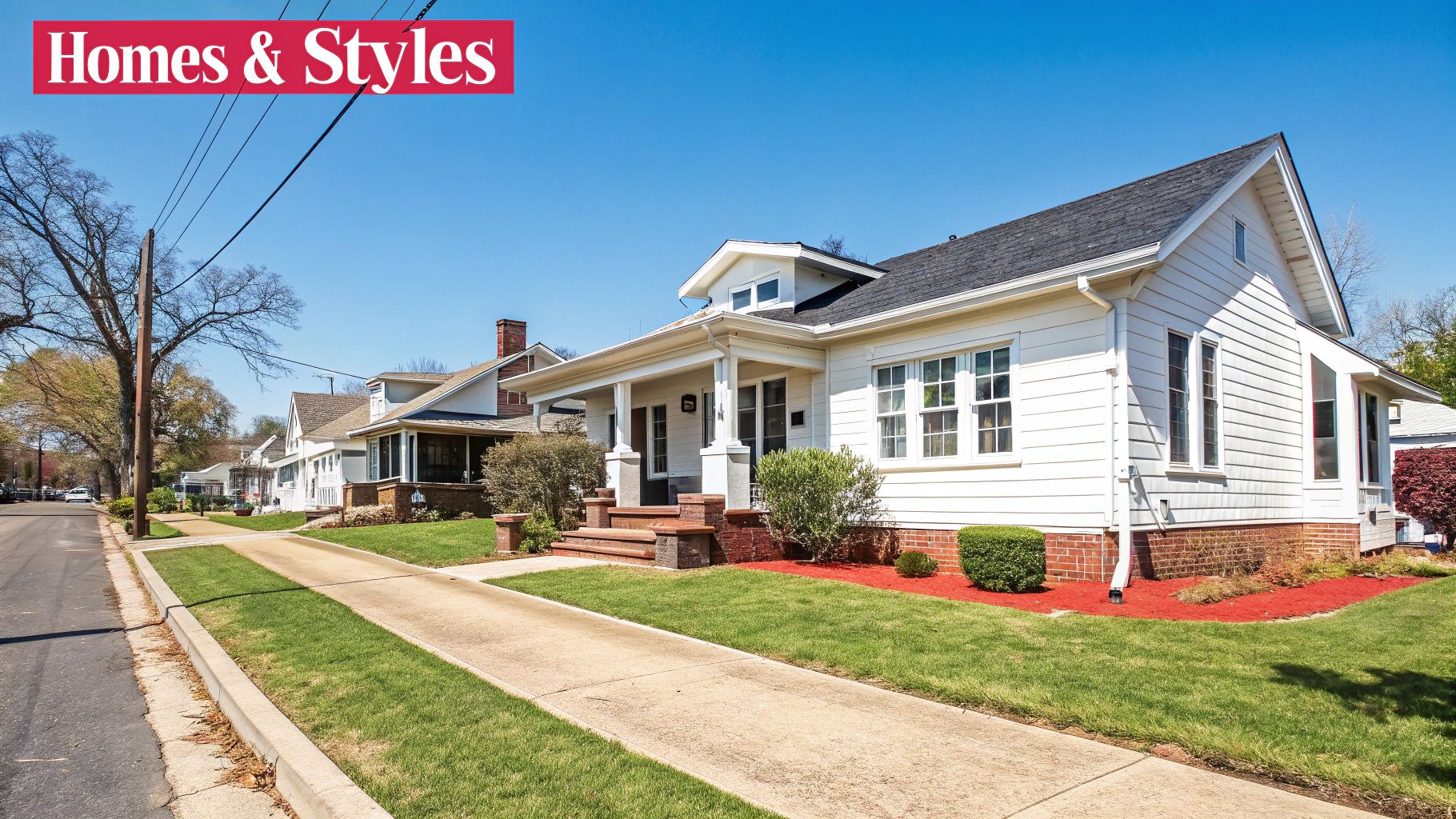 A sunny residential street featuring white houses with green lawns and a clear blue sky.