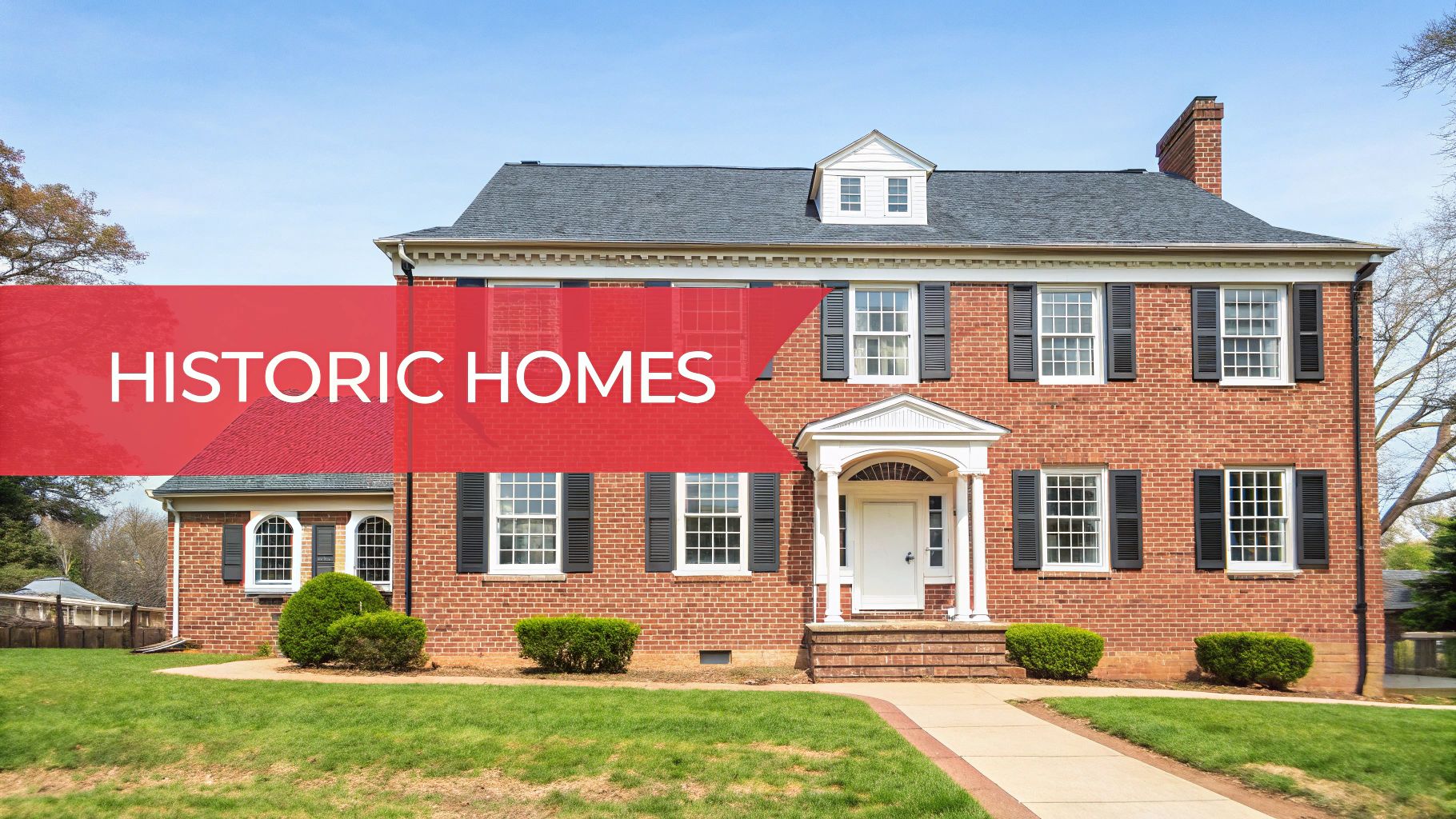 A large, traditional red brick house with black shutters and a white front door, featuring a red banner reading 'HISTORIC HOMES'.