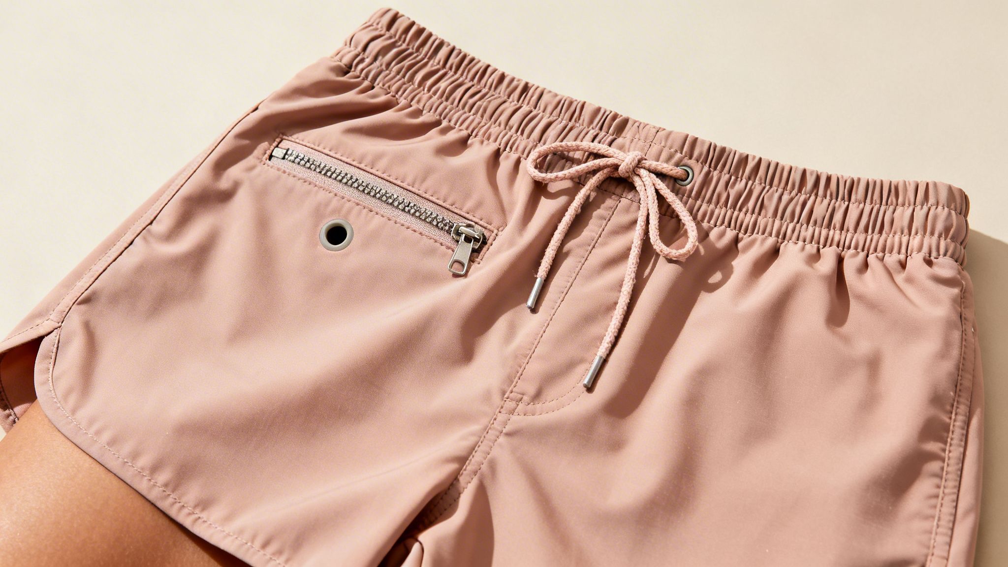 Close-up of light pink women's board shorts featuring an elastic waist, drawstring, and zippered pocket.