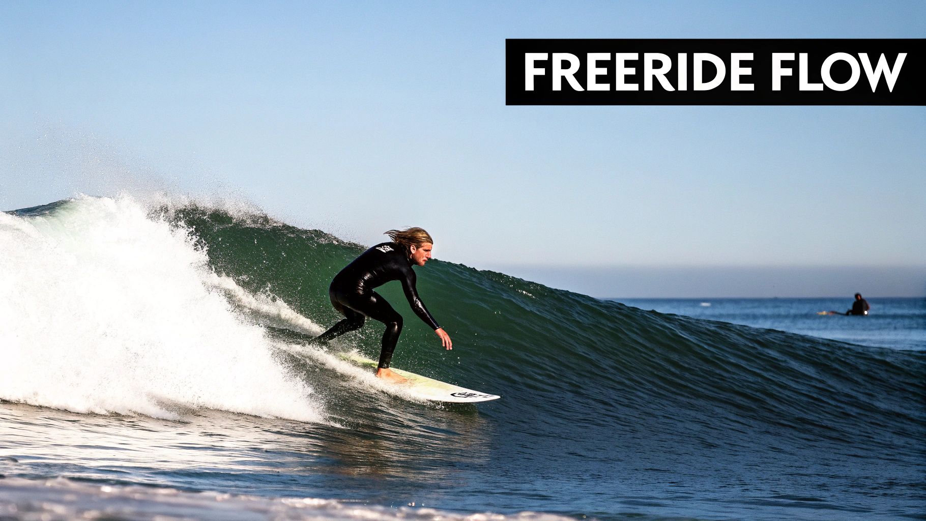 A male surfer rides a powerful wave, generating white spray, under a clear sky.