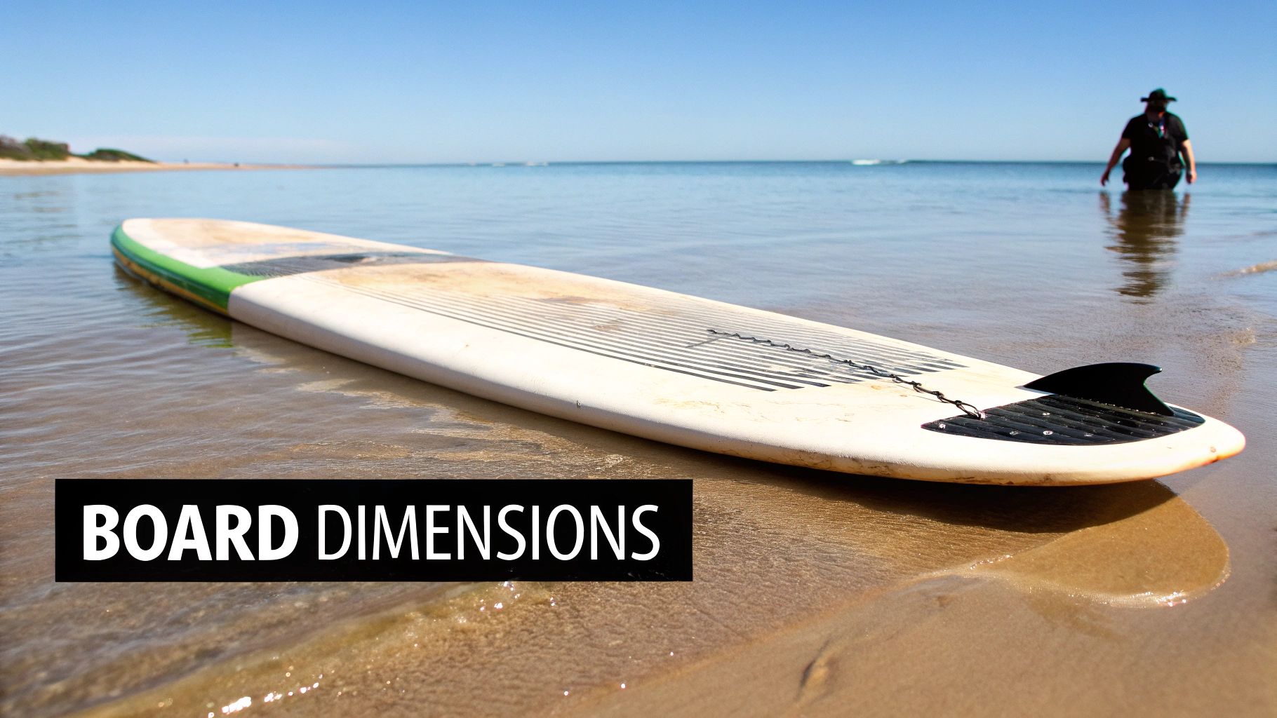 A white and green stand-up paddleboard rests on the sandy beach at the ocean's edge.