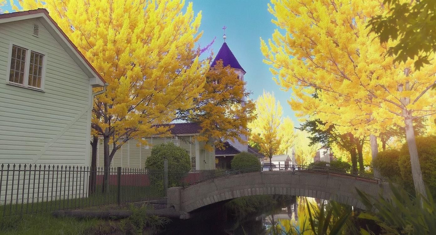 Et naturskønt efterårsscene med livlige gule træer, et hus, en kirke og en stenbro over en stille kanal.
