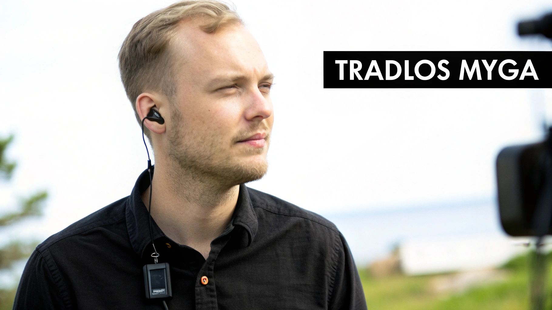 En mand med lyst hår bærer en in-ear høretelefon og en trådløs mikrofon på sin sorte skjorte.