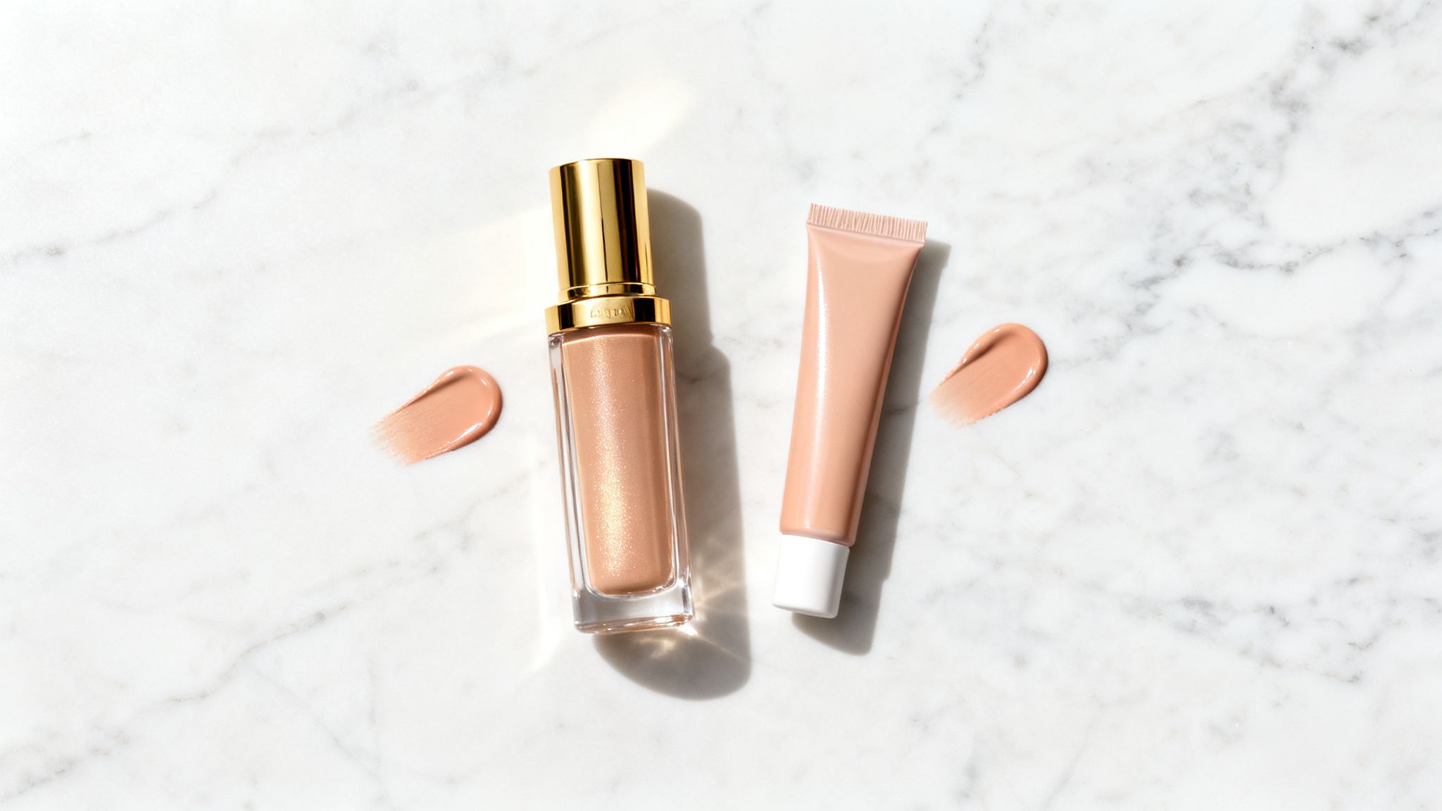 Two peach-toned liquid makeup products, a bottle and a tube, with swatches on white marble.