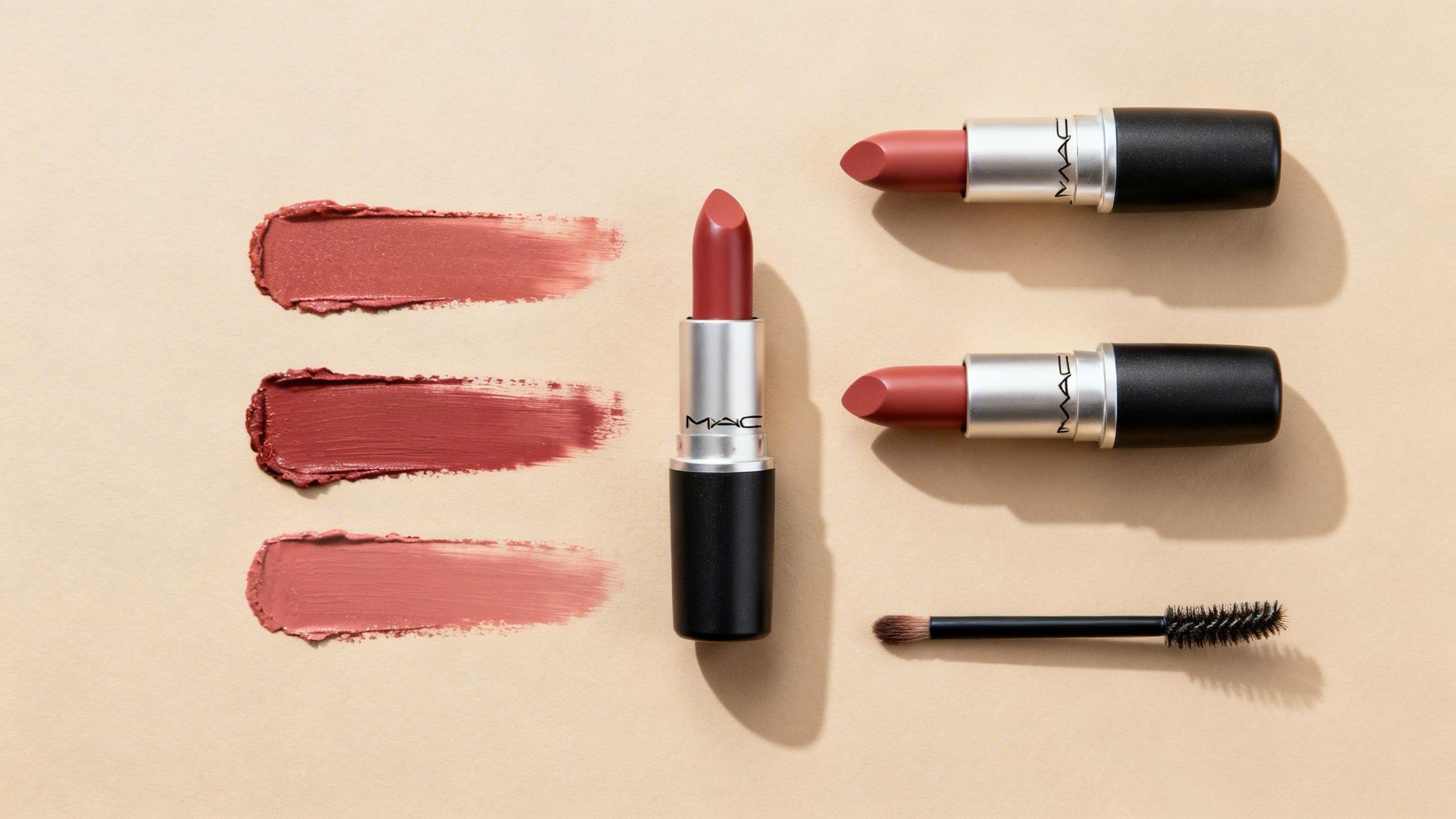 Three MAC lipsticks displayed with corresponding swatches in various red and nude shades on a beige surface.