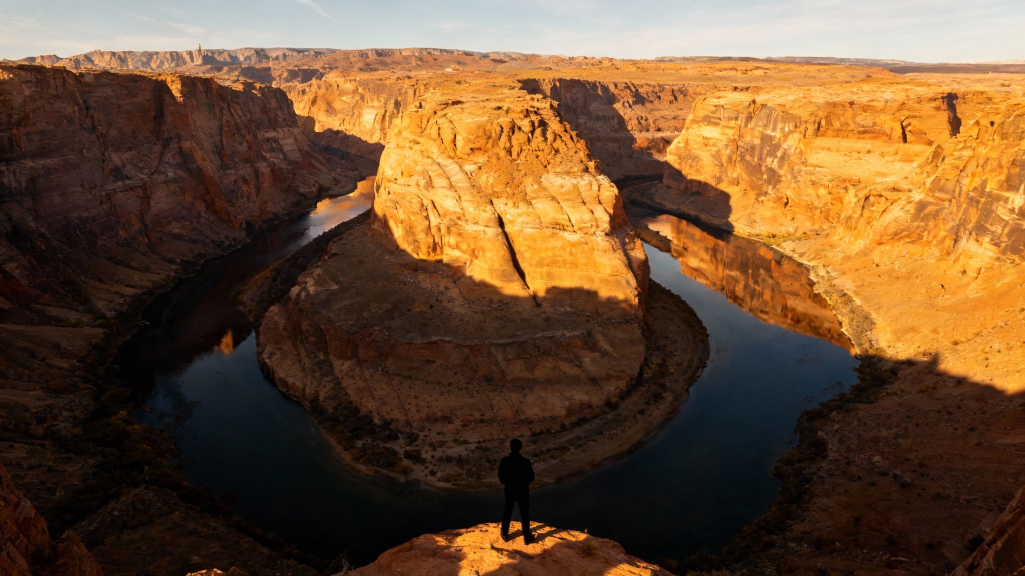 A lone figure stands overlooking the majestic Horseshoe Bend at sunset, with the Colorado River.