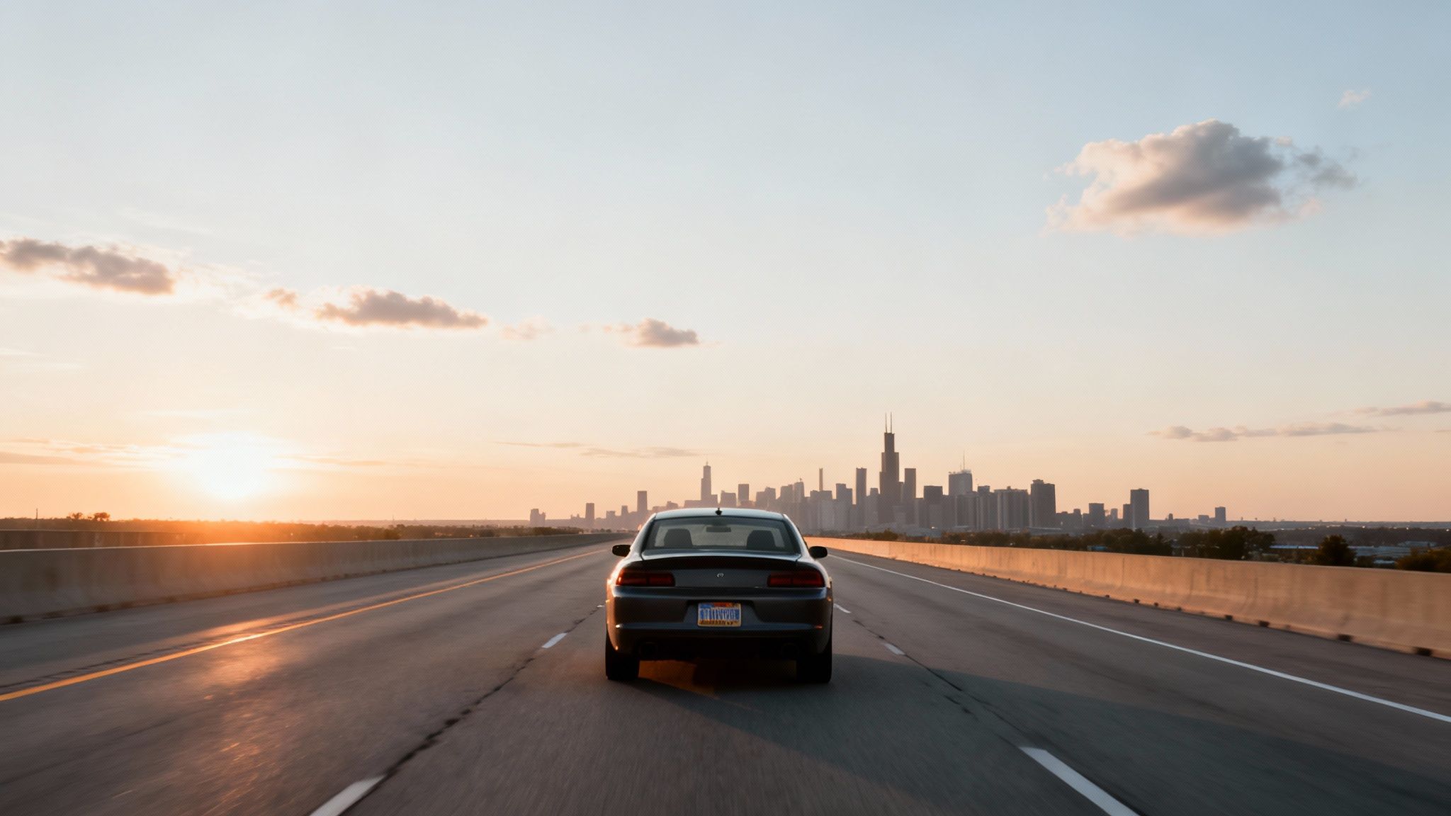 Rear view of a car driving on a highway towards the Chicago skyline at sunset.