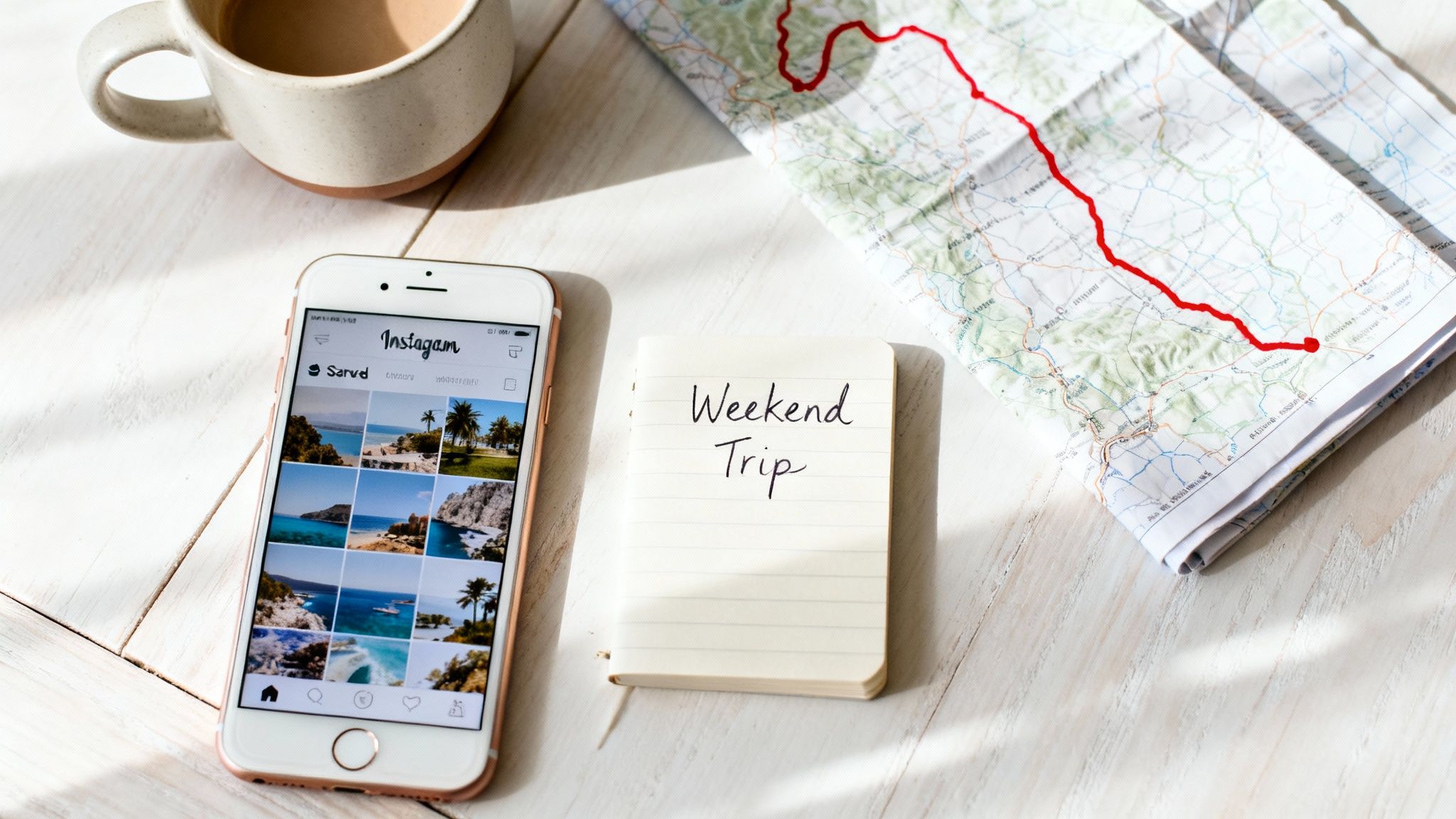 Overhead shot of a phone showing travel photos, a map, and a 'Weekend Trip' notebook.