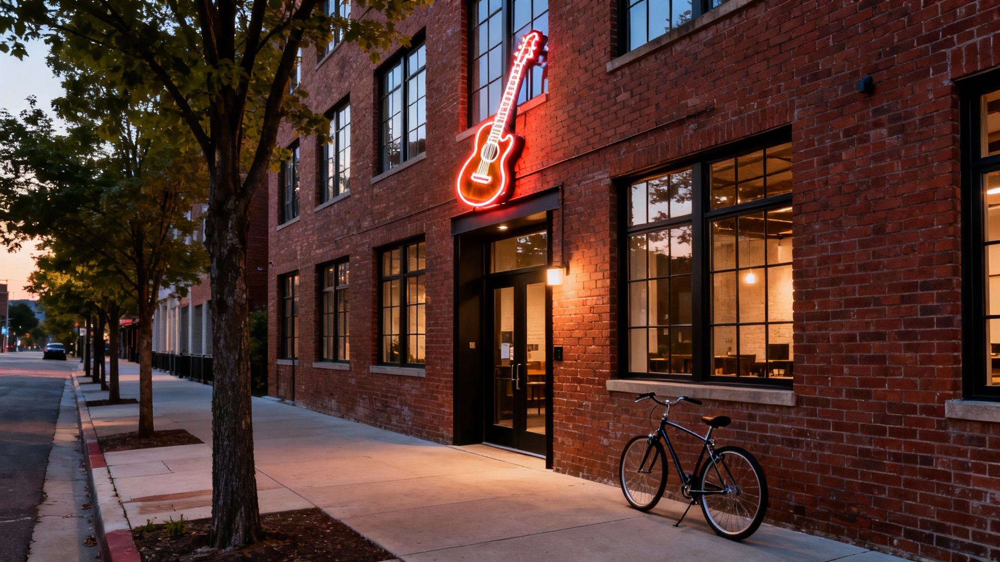 Modern brick building at dusk featuring a vibrant neon guitar sign above the entrance, with a bicycle parked.