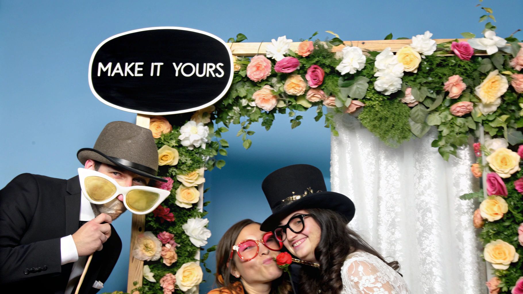 A stylish wedding photo booth with a custom floral backdrop and unique props.