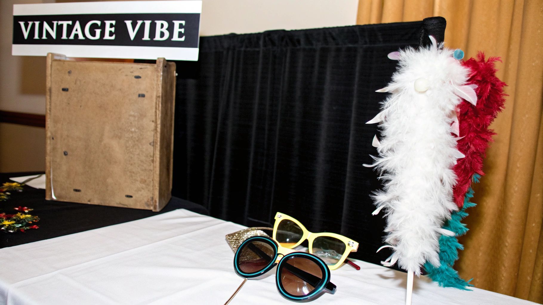 A vintage vibe photo booth setup with a sign, feather boas, and two pairs of retro sunglasses.