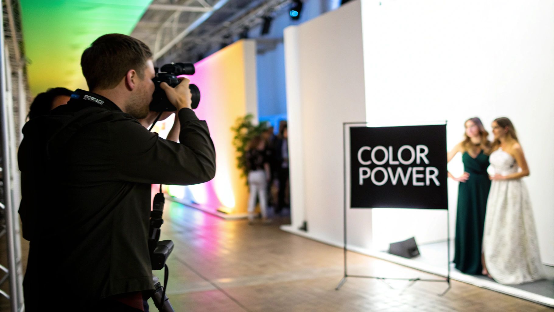 A photographer captures two women posing in elegant dresses at an event with colorful lighting.