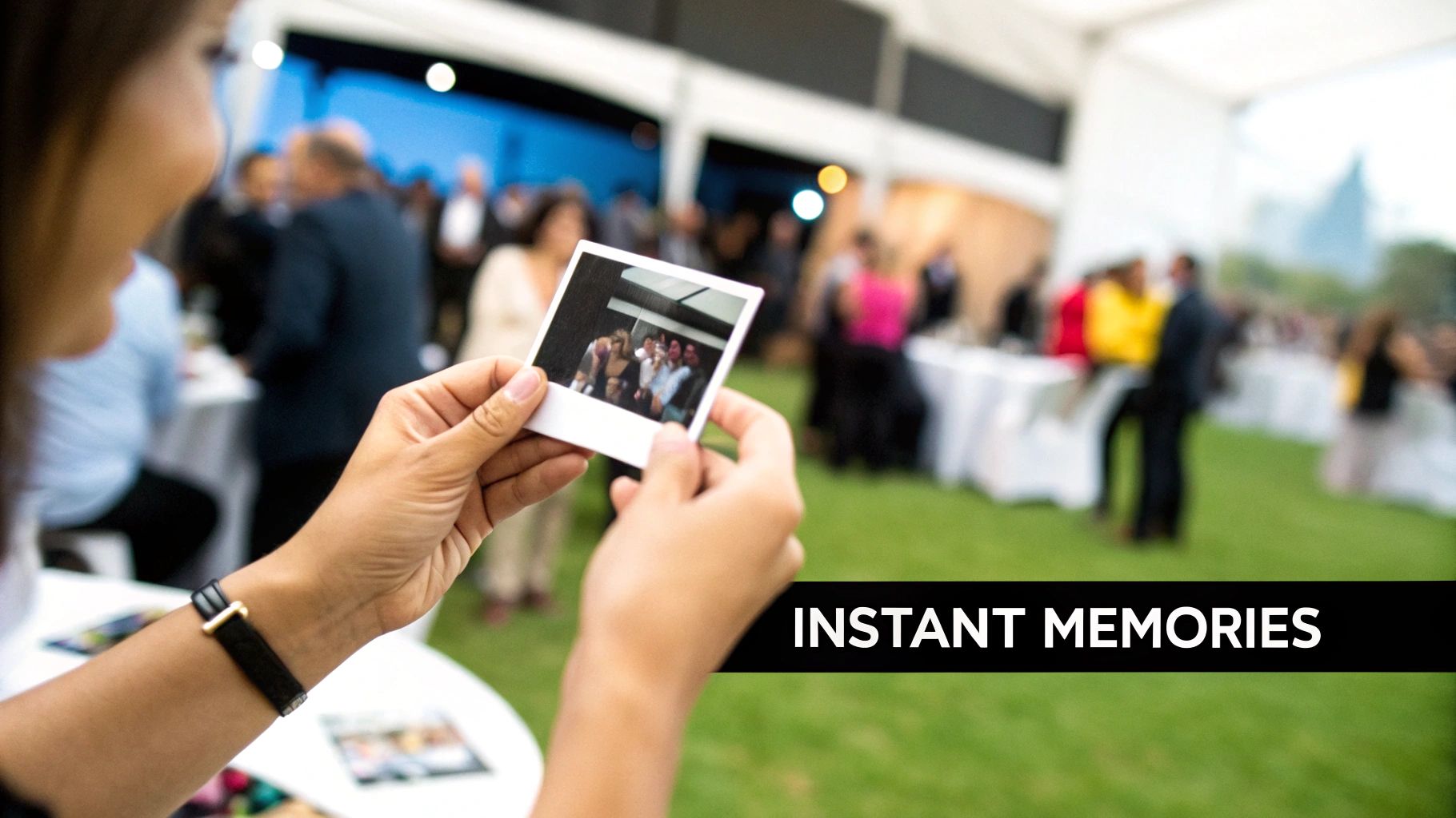 A person holds up an instant photo of friends smiling at an outdoor event.