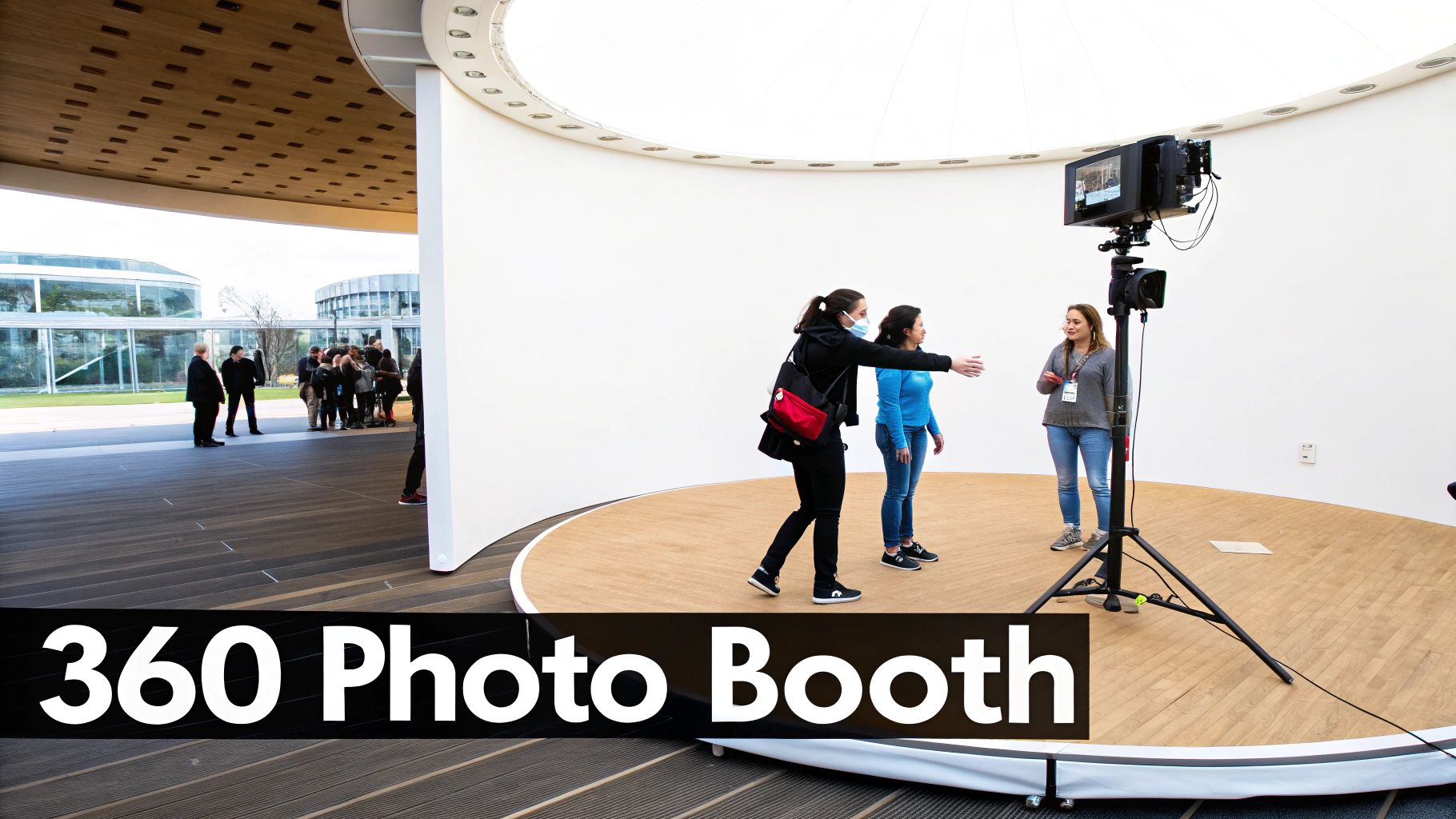 Women posing at a 360 photo booth with a camera and monitor on a circular wooden stage.