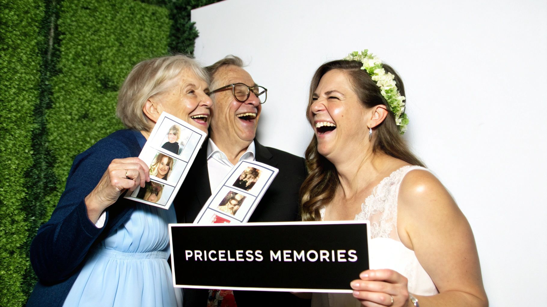 Three generations of a family joyfully laughing with photo booth strips at a wedding.