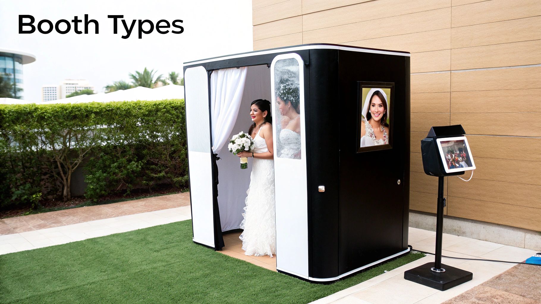 An elegant bride in a white gown exits a black and white photo booth outdoors.