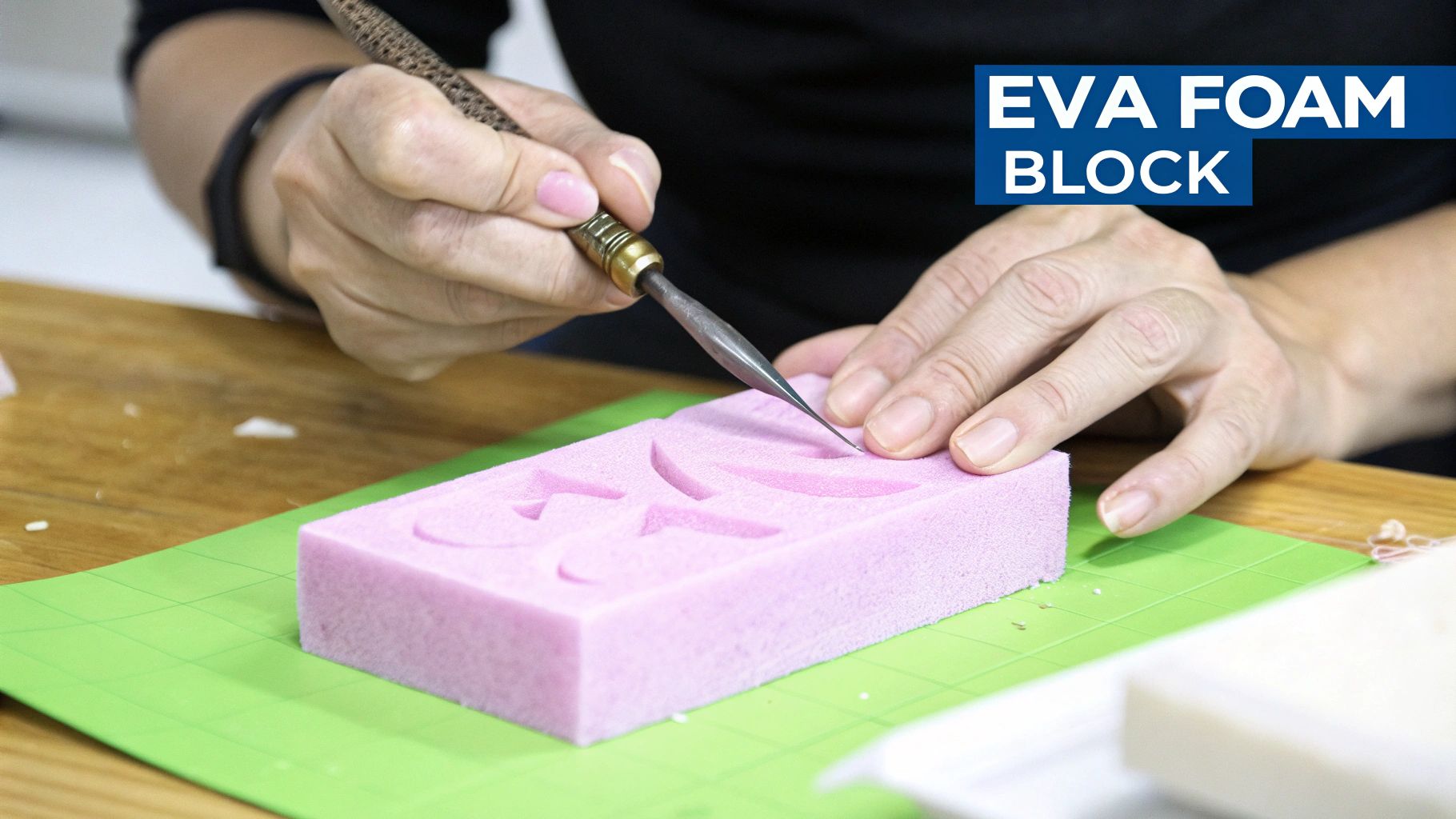 A person's hands delicately carve a floral design into a pink EVA foam block using a sharp tool.