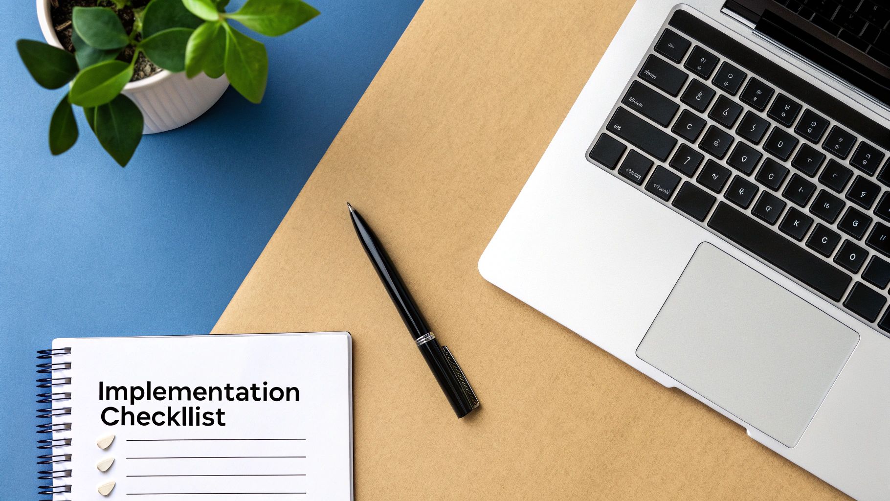 Top-down view of a workspace with a laptop, 'Implementation Checklist' notebook, pen, and plant.