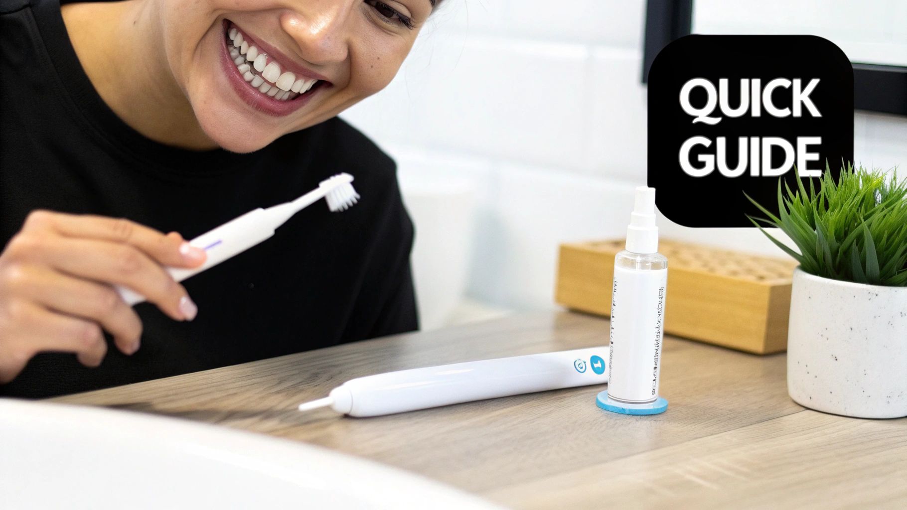A happy woman holding a white electric toothbrush smiles, with other dental care items on a wooden counter.