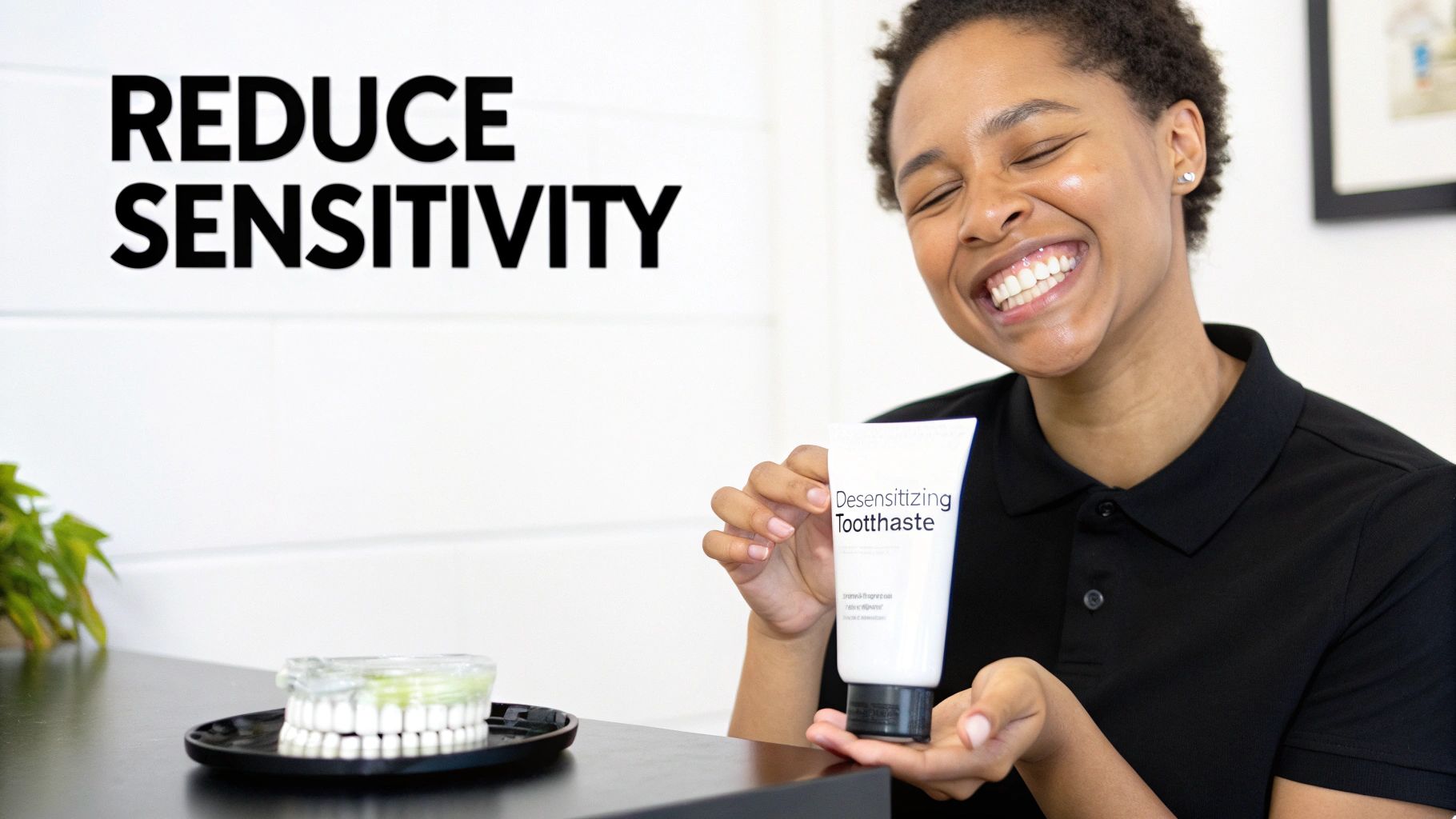 A smiling person holds desensitizing toothpaste, with a dental model nearby, promoting reduced sensitivity.