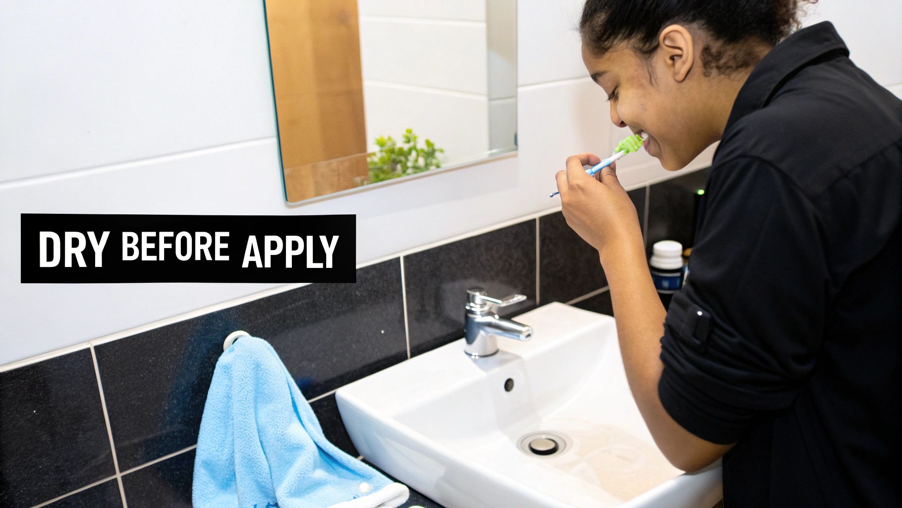 A smiling person brushing their teeth with a green toothbrush in a bathroom, near a sink.