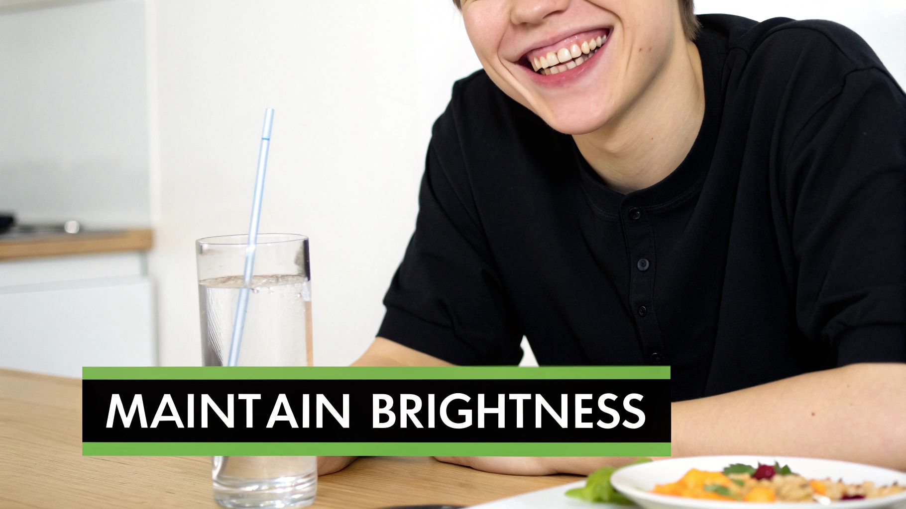 A smiling person with bright teeth, sitting at a table with a glass of water and a healthy meal.