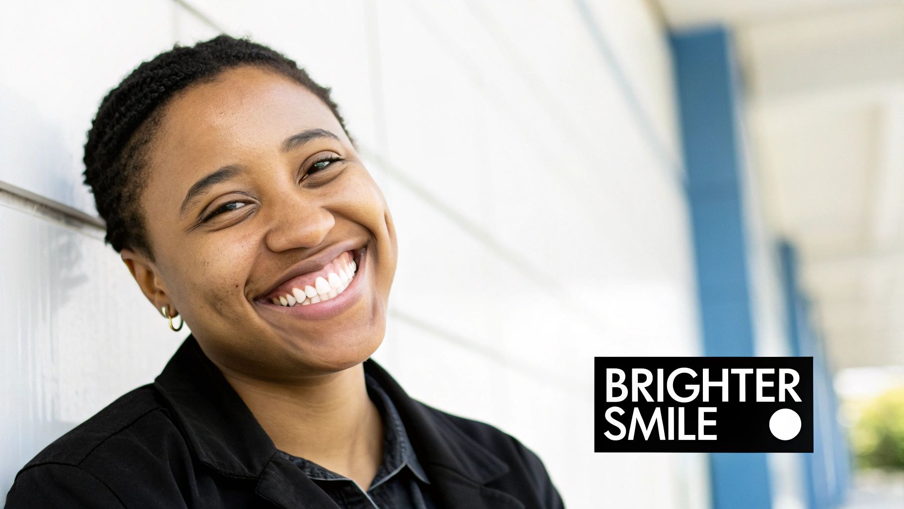 A young woman with short curly hair smiles widely, revealing her bright, white teeth, with 'BRIGHTER SMILE' text.