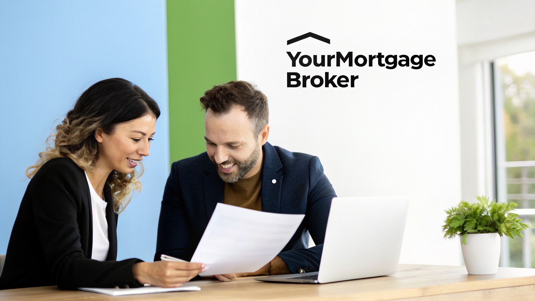 Two smiling mortgage brokers reviewing documents at a desk with a laptop and plant.