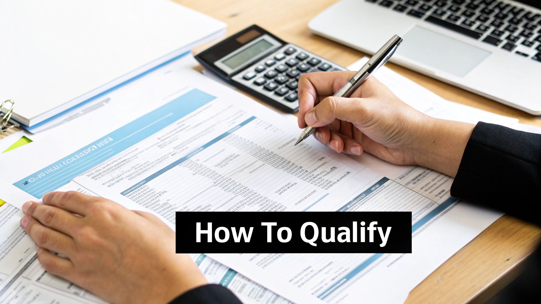 Hands writing on a financial document with a pen, calculator, and laptop, illustrating qualifying criteria.
