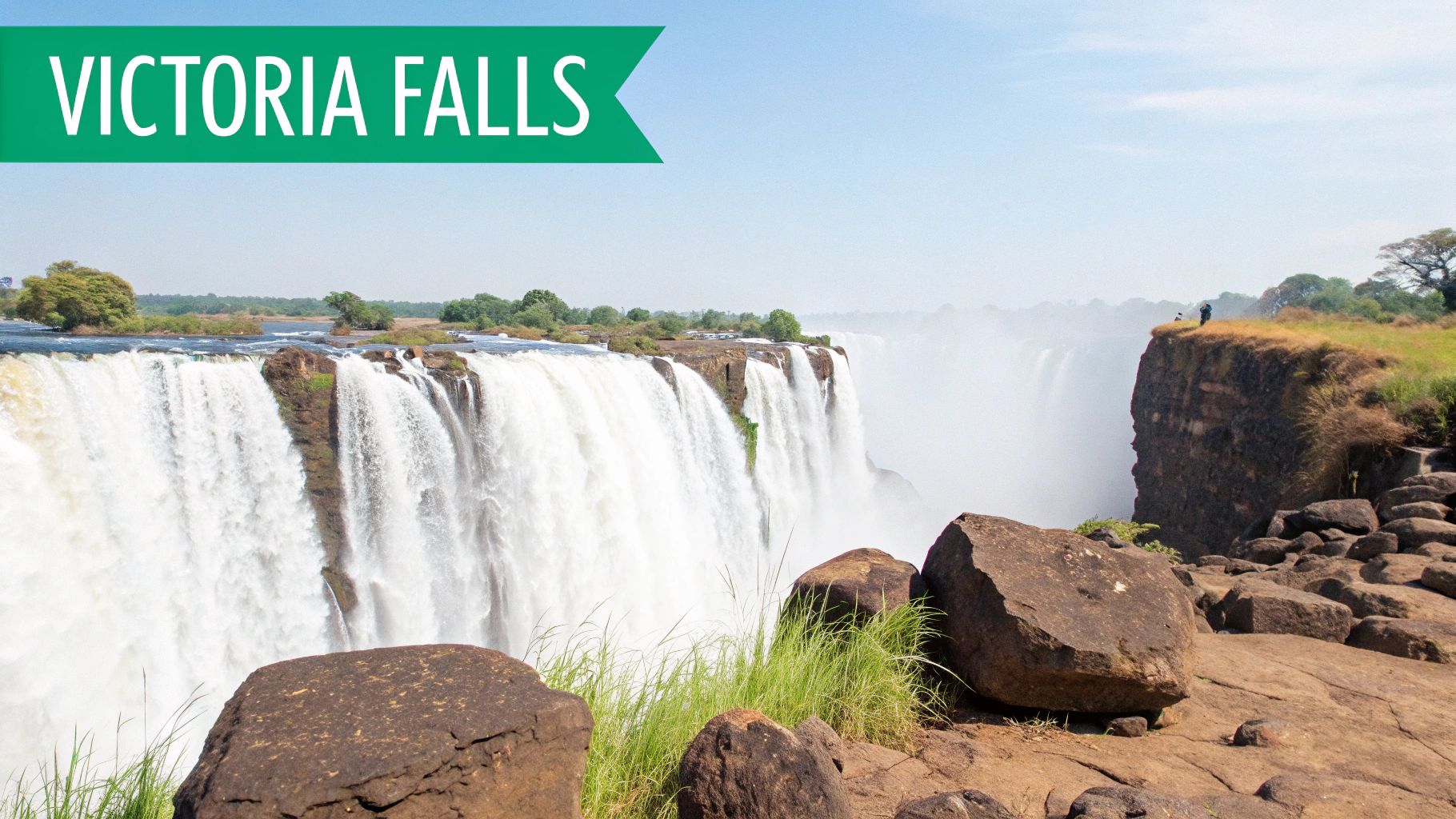 Majestic Victoria Falls with powerful water cascades, rising mist, and a person on a distant cliff.