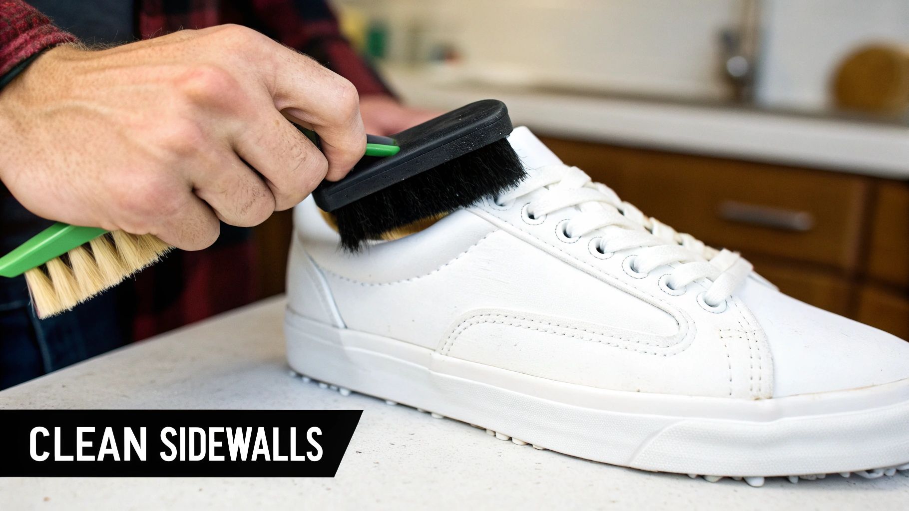 A person uses two brushes to clean the white sidewalls of a sneaker on a countertop.